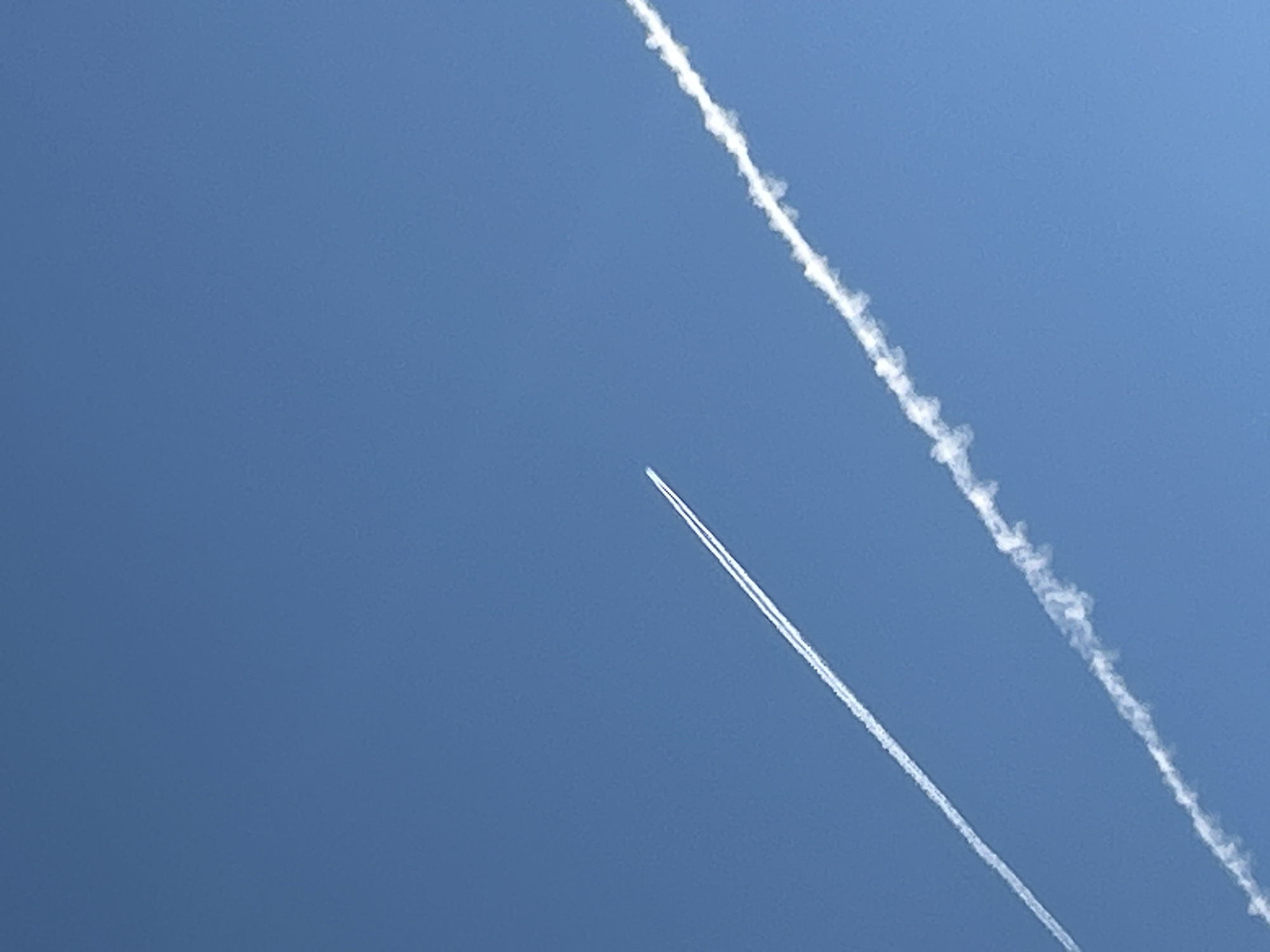 Two contrails stretch across a clear blue sky. The contrail on the left is thinner and straighter, suggesting a higher-flying aircraft. The contrail on the right is wider and more fragmented, indicating a lower altitude or different atmospheric conditions. Both contrails are white against the uniform blue background. There is no indication of the city of Matraevo, Russia, or any other geographical features in the image.