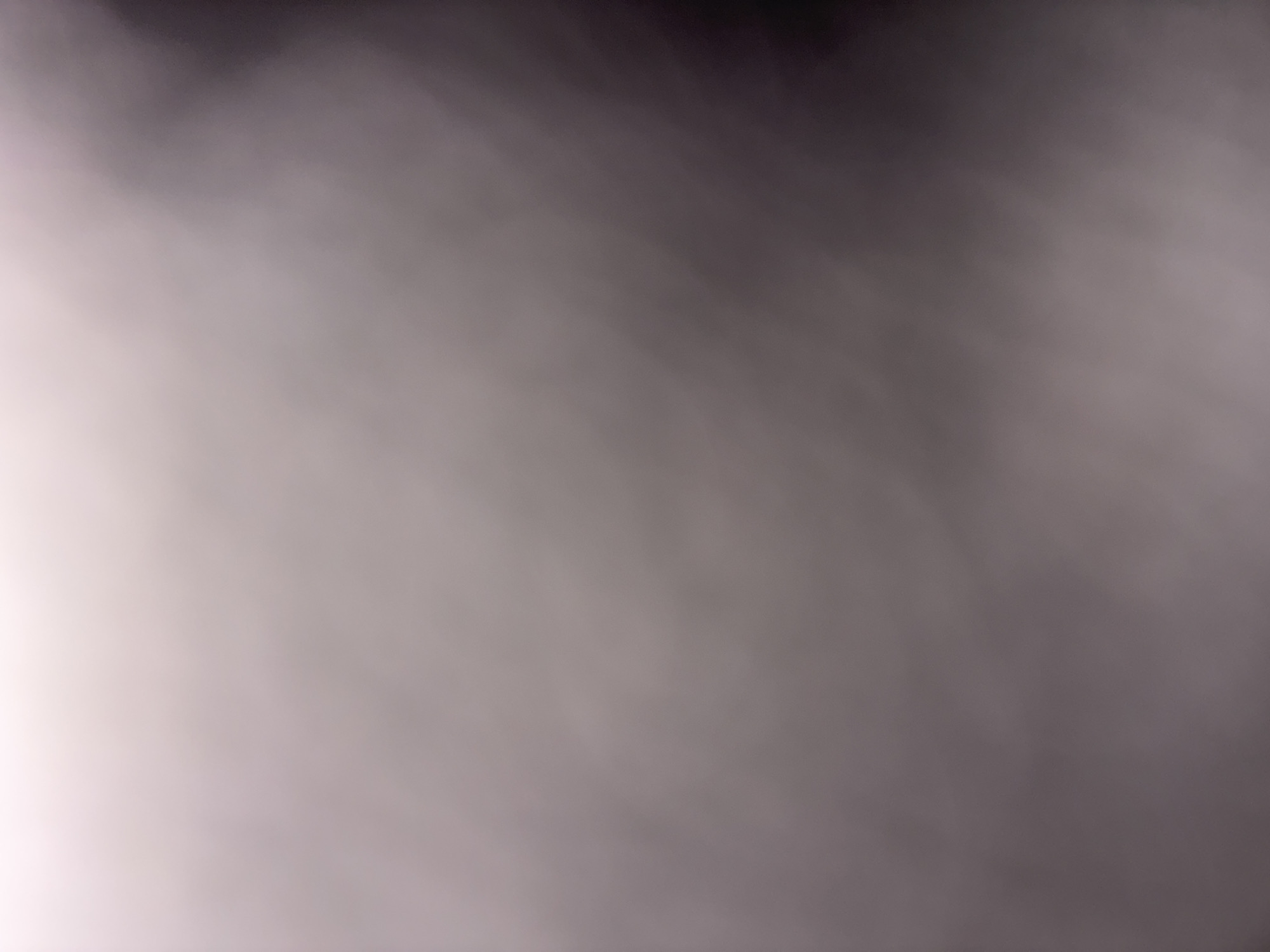 This is an abstract, out-of-focus image. There are no discernible people, subjects, objects, or actions. The environment appears to be dimly lit with a gradient of light from a bright, white-toned area on the left to a dark, purplish-toned area on the right. There are subtle, swirling patterns within the gradient. No location in Plovdiv, Bulgaria, or any other specific geographic information can be determined from this image.