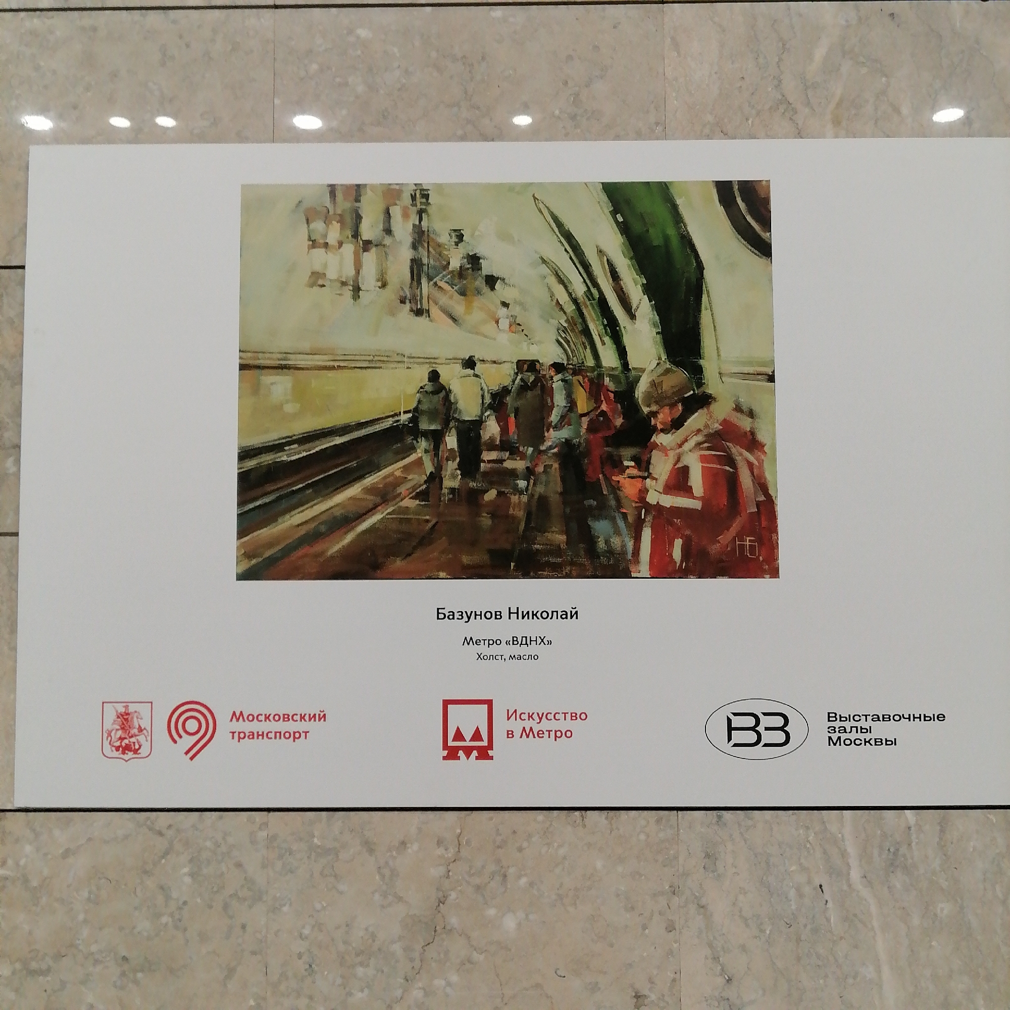 The image shows a sign with a painting on it, placed on a marble or tiled surface. The painting depicts the interior of the VDNKh metro station in Moscow, Russia. The painting appears to be an impressionistic depiction of people riding an escalator in the metro station. The sign also includes the name of the artist, "Базунов Николай" (Bazunov Nikolai), the title of the painting "Метро «ВДНХ»" (Metro "VDNKh"), and the medium "Холст, масло" (Canvas, oil). The sign also includes logos for "Московский транспорт" (Moscow Transport), "Искусство в Метро" (Art in the Metro), and "B3 Выставочные залы Москвы" (B3 Exhibition Halls of Moscow).