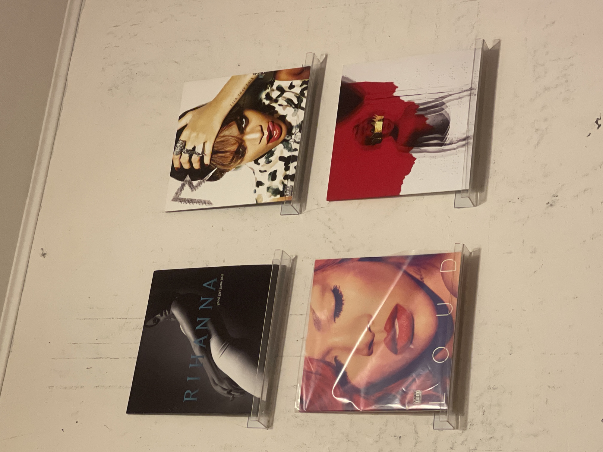 The image shows four Rihanna albums mounted on a light-colored wall. The albums are "Talk That Talk", "Unapologetic", "Good Girl Gone Bad", and "Loud". The albums are displayed in clear plastic frames, arranged in a two-by-two grid. The wall has a slightly textured surface. There is no indication of location in the city of Khimki, Russia, or any other specific location.