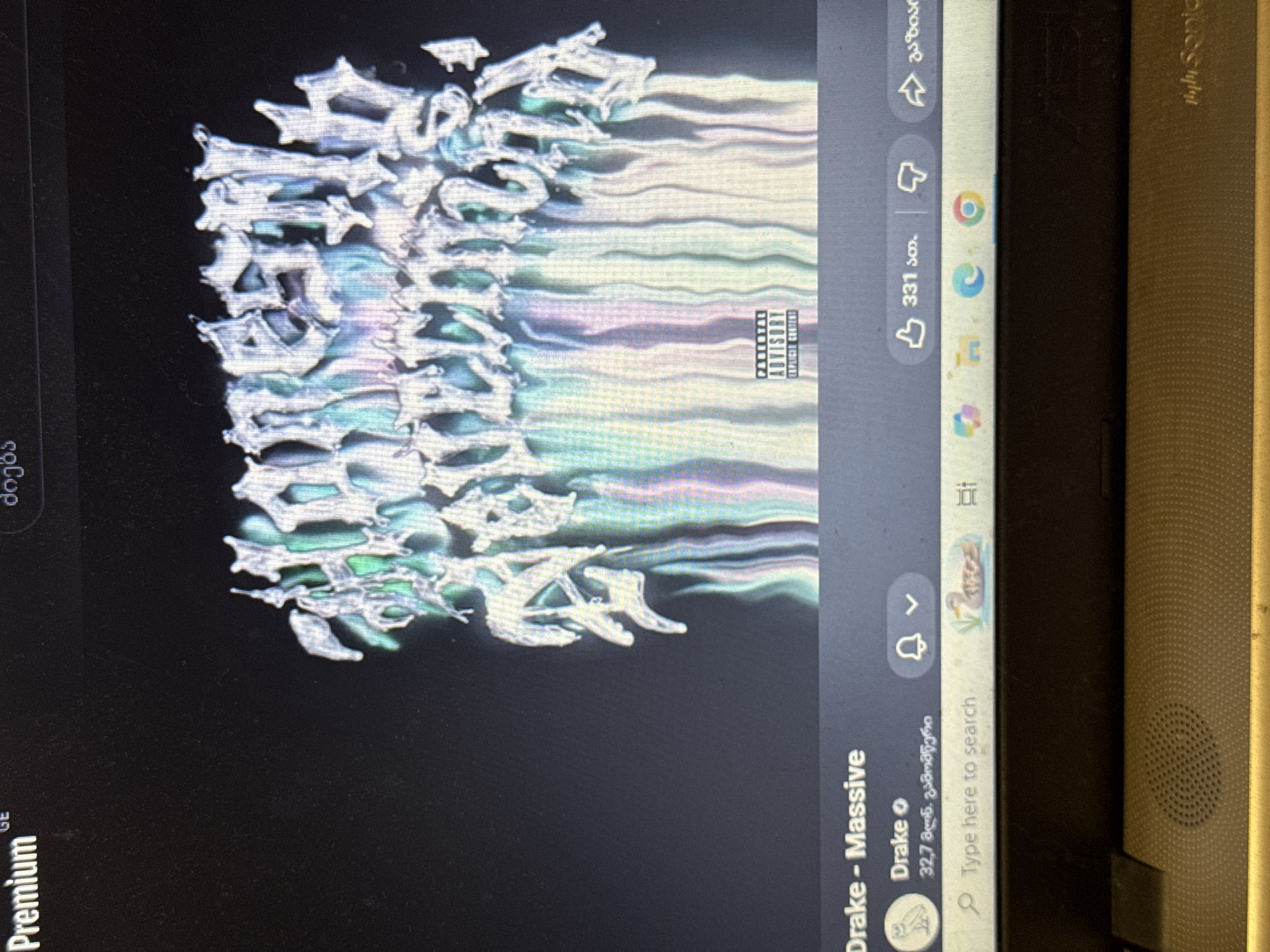 The image is a screenshot of a computer screen displaying a music video or song page. The title of the song is "Drake - Massive". Above the title, there is album art with the words "honestly, nevermind" in a metallic, dripping font, colored in iridescent greens and blues. A "PARENTAL ADVISORY EXPLICIT CONTENT" label is visible on the album art. Below the title, the artist "Drake" is listed, along with a follower count in Georgian script ("32,7 მილ. გამოხმაური"). Several interface icons are visible, including a notification bell, a thumbs-up icon with the number "331", a thumbs-down icon, and a share icon. A search bar with the text "Type here to search" is at the bottom of the screen. The environment appears to be indoors, with a laptop visible in the foreground. The exact location in the city of Unknown, Unknown is not determinable from the image.