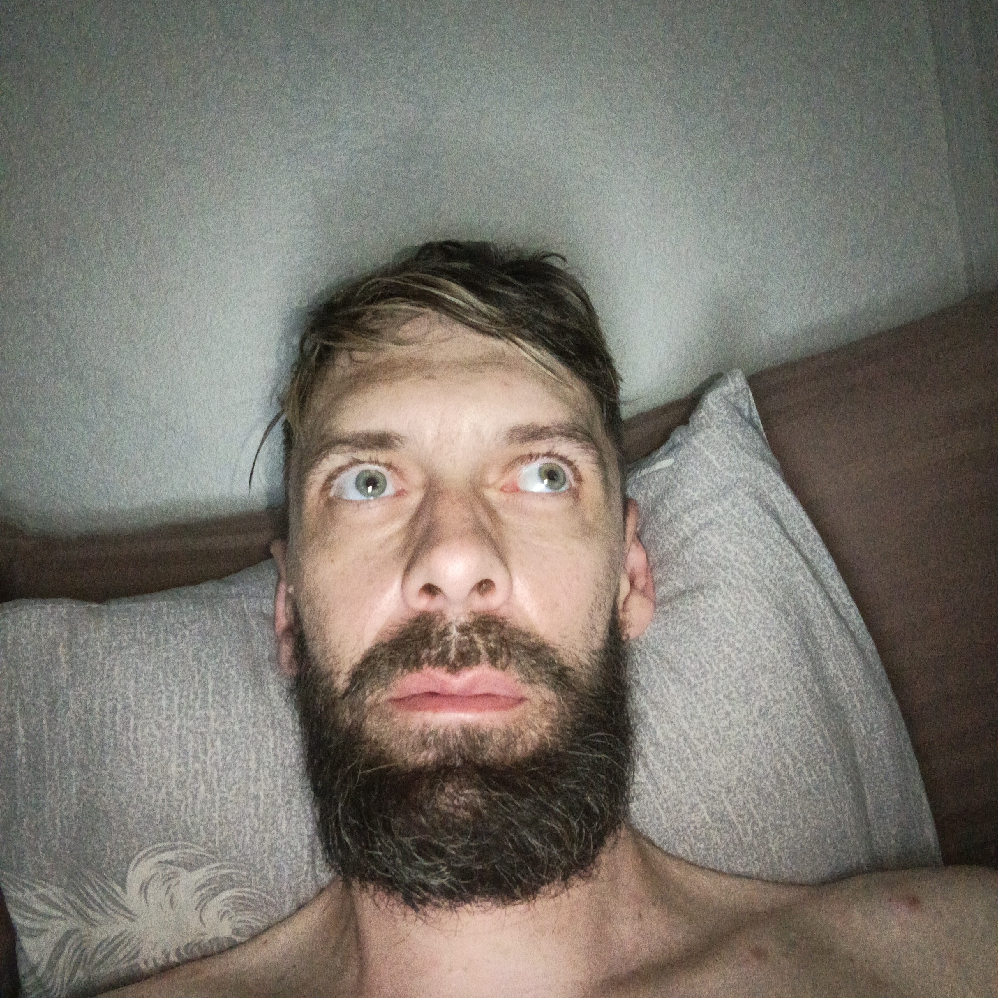 A man with light skin, green eyes, and a beard lies on a pillow, looking upwards. His hair is light brown with blonde streaks. He appears to be in a bed, against a headboard. The background is a pale wall. The image was presumably taken indoors. Марковский, Russia is not evident in the picture.