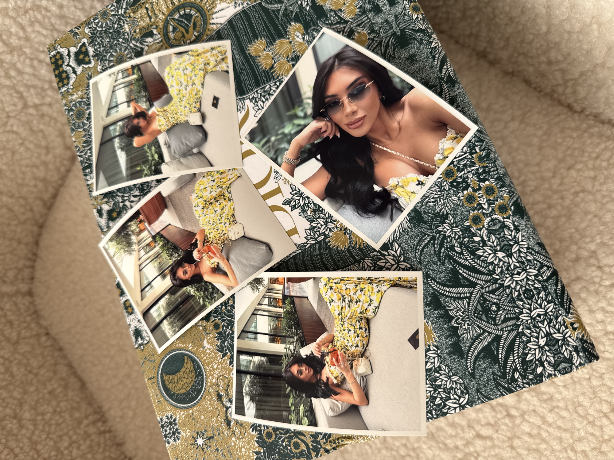 The image shows a flat lay of four printed photographs arranged on a patterned box, which is placed on a textured, beige surface. The photographs feature a young woman with dark hair, wearing a yellow floral dress. In some photos, she is holding a drink with a straw, and in others, she is posing with her hands on her head or touching her face. The box has a dark green and gold pattern with floral and celestial motifs. The overall scene is dimly lit. There is no information about the city of Plovdiv, Bulgaria in the image.