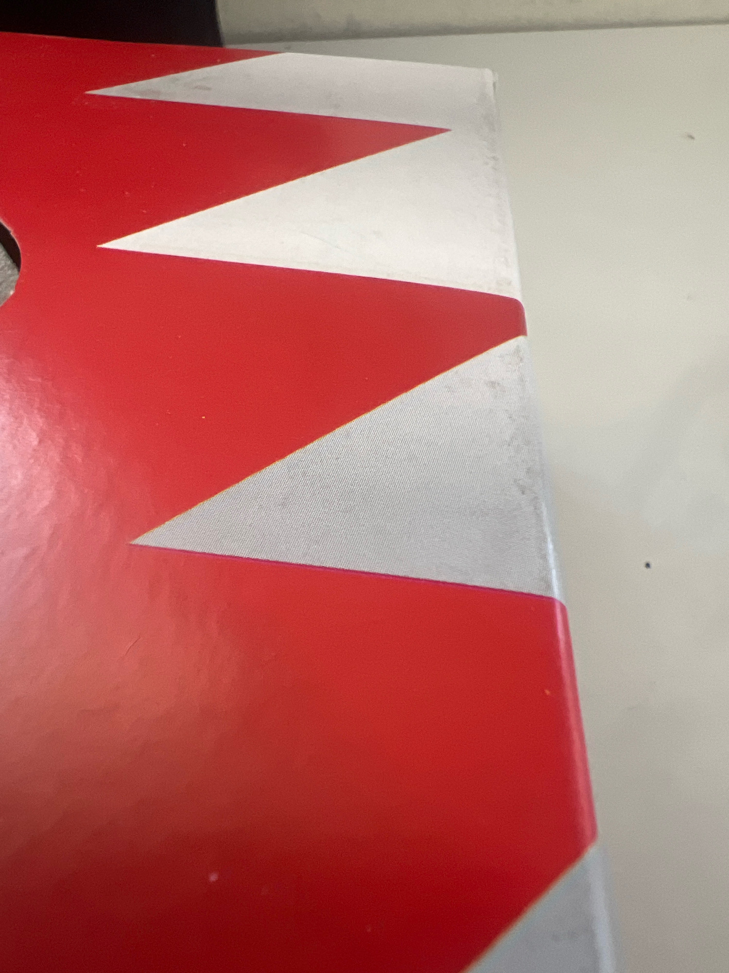 A close-up, slightly angled, top-down view of a portion of a red and white striped object. The stripes are angled and appear to form a chevron pattern. The object's surface is textured and shows some scuff marks and dust, particularly along the edge. The background is a light, neutral color, suggesting it is a flat surface like a table or wall. No people or specific landmarks are visible, and the location in the city of صدد, Bahrain, is not discernible from the image itself.