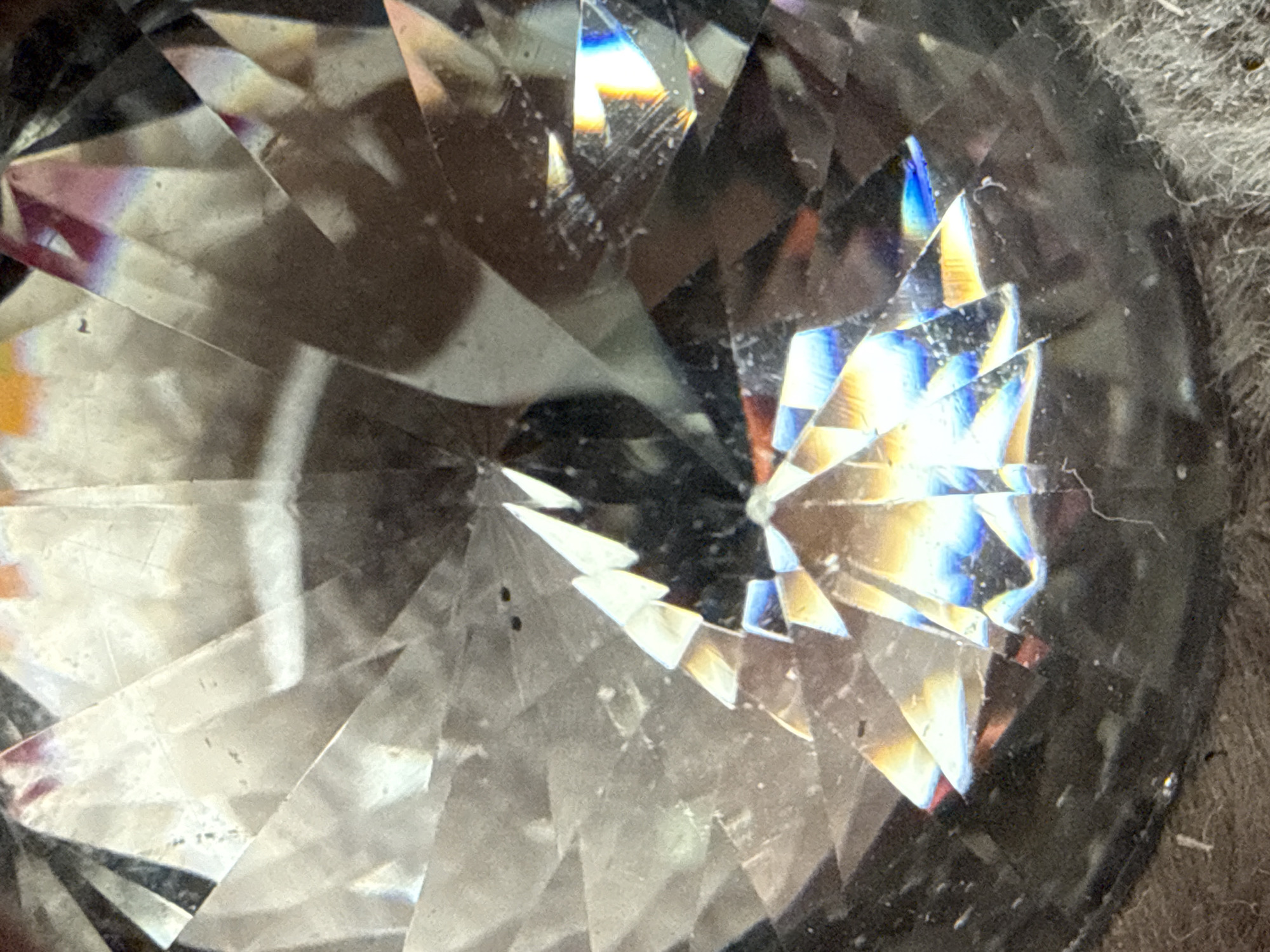 The image shows a close-up view of a cut glass or crystal object, likely a decorative piece. The facets of the object create a complex pattern of light and shadow, with iridescent reflections visible. The object appears to be sitting on a textured surface that may be slightly dusty or dirty. There is no indication of the location or city. No people or actions are visible in the image.
