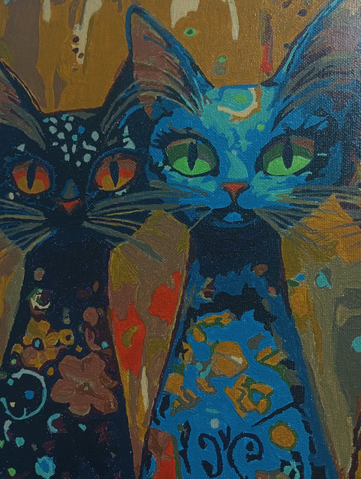 Two stylized cats are depicted in an oil painting style. The cat on the left is rendered in shades of dark blue and black, with orange eyes and small, light blue or turquoise spots scattered across its fur. The cat on the right is primarily blue, with green eyes and orange floral patterns on its chest. Both cats appear to be wearing bibs or vests with floral designs and are set against a backdrop of yellow and brown tones. The artwork does not provide information to identify if the location is in the city of Pervomaysky, Russia.