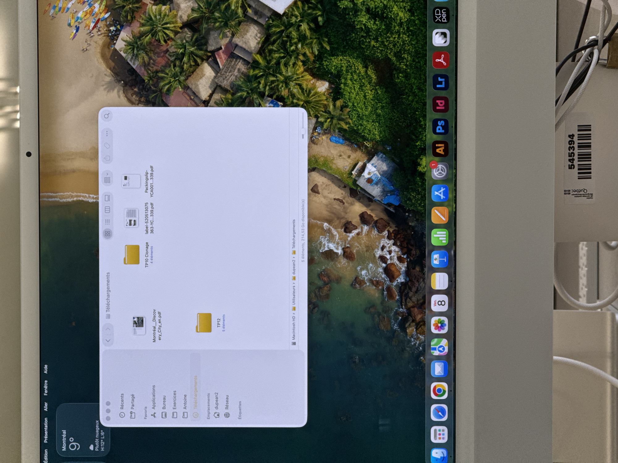 The image shows a screen capture of a desktop, with a Finder window open displaying a list of downloaded files. The Finder window is titled "Téléchargements," which translates to "Downloads" in English. The files listed include PDFs such as "Montréal_Discovery_City_en.pdf," "label-520513075-363-YC...339.pdf," and "Packingslip-YCA001...339.pdf," as well as folders named "TP10 Clonage" and "TP12."
The Finder window is superimposed over a desktop background that appears to be an aerial view of a tropical beach with palm trees, buildings, and ocean. A dock with application icons is visible on the side of the screen. Icons for applications such as Adobe Photoshop, Illustrator, InDesign, Lightroom, and others are present.
In the bottom left corner of the screen, a weather widget displays the current weather in Montreal, Canada, with a temperature of 9°C and a forecast of "Plutôt nuageux" (mostly cloudy).
On the right side of the image, there is a partial view of a white-colored electronic device, possibly a monitor, with a sticker showing the number "545394." The word "Québec" is also visible.
