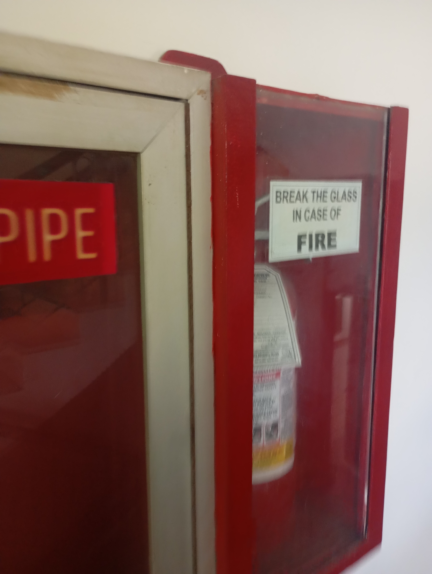 The image shows a red fire extinguisher cabinet with a sign that reads "BREAK THE GLASS IN CASE OF FIRE". Next to it is a cabinet with a red label that says "PIPE". The scene appears to be inside a building in Davao City, Philippines.