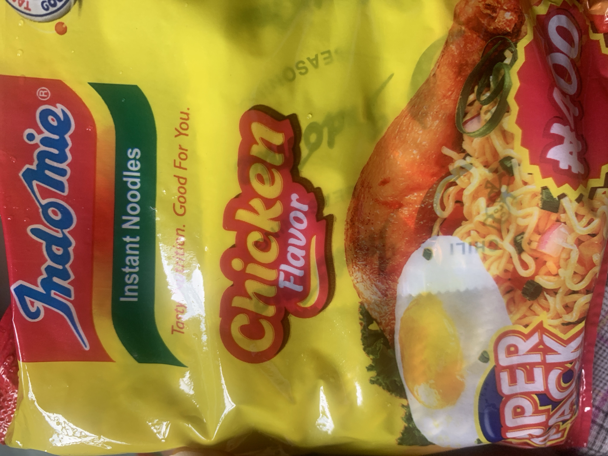 The image displays a close-up of a yellow Indomie instant noodles packet. The prominent branding includes the "Indomie" logo in blue and red, with "Instant Noodles" written below it. Further down, the flavor "Chicken" is highlighted in a red and yellow stylized font, with "Flavor" in white underneath. The packaging also features an illustration of a fried egg, a cooked chicken leg, and a portion of noodles garnished with green chili rings. The bottom left corner shows "SUPER PACK" in large white letters on a blue and red background, and the bottom right displays "400" in large white numbers with a currency symbol that appears to be the Nigerian Naira. The packet is slightly crinkled, suggesting it is a retail product. The background is a plain yellow from the packaging. There are no people or environmental details that would indicate a specific location in Jalingo, Nigeria.