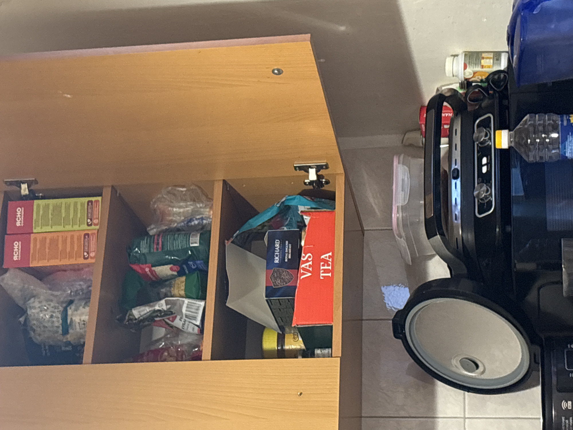 The image shows an open kitchen cabinet. Inside, there are boxes of tea, pasta, and other food items. Next to the cabinet is a countertop oven, a water bottle, and other items. There is no information present to determine the location in Murino, Russia.