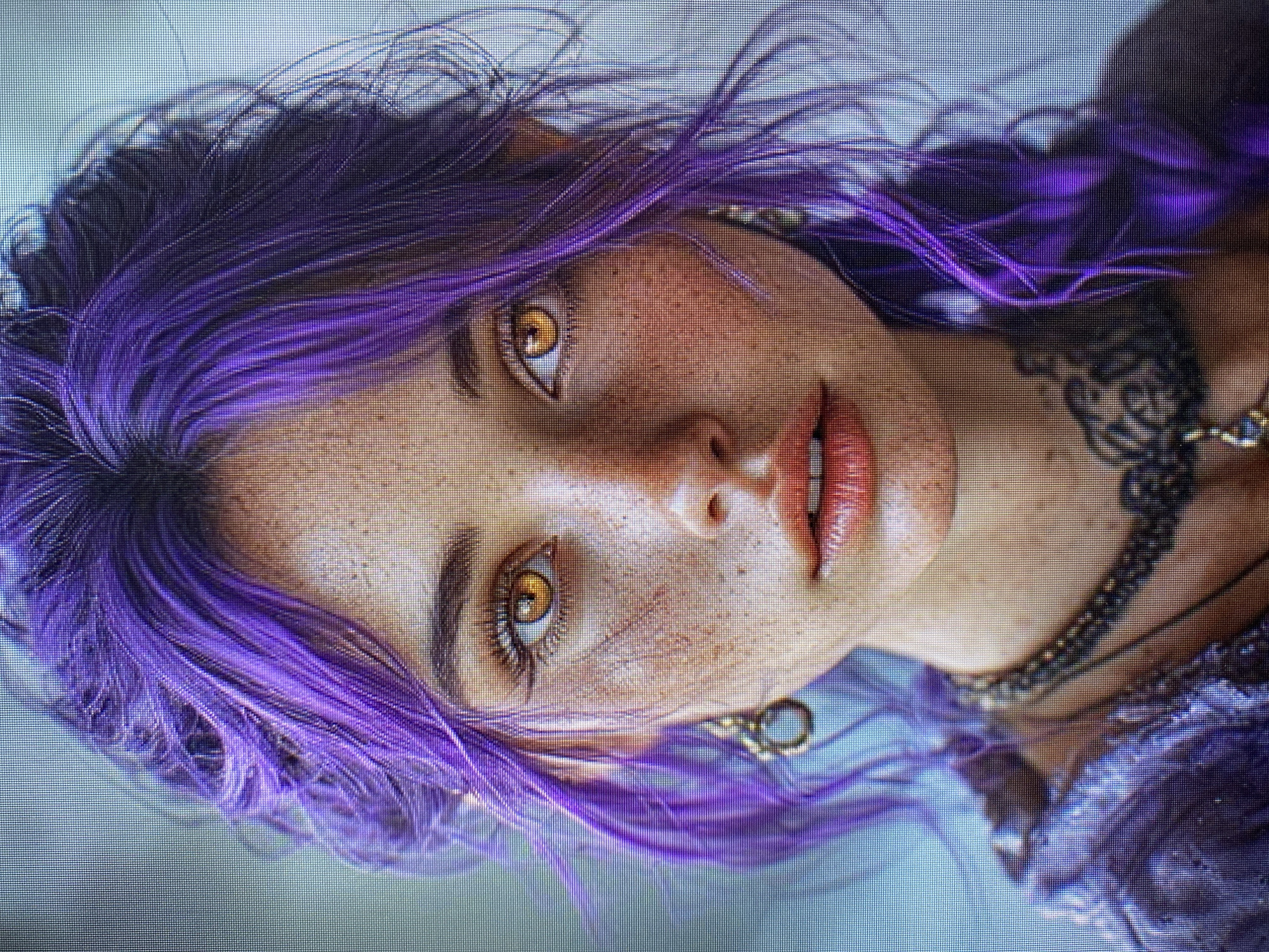 The media file is a close-up, digitally rendered image of a young woman with striking purple hair, styled in loose braids and wisps that frame her face. Her skin is fair and adorned with freckles across her nose and cheeks. She has large, amber-colored eyes with prominent lashes, and her lips are slightly parted, revealing a hint of her teeth. The woman is wearing a dark, intricately designed choker necklace, and a glimpse of a furry, purple garment is visible on her right side. Her head is tilted, and she is looking directly at the viewer with a neutral to slightly curious expression. The background is a soft, blurry blue-grey, providing no specific setting cues. The image appears to be a portrait or character concept, likely from a video game or digital art project. There is no visible text in the image. The location context of Yerevan, Armenia, is not visually discernible from the image itself.