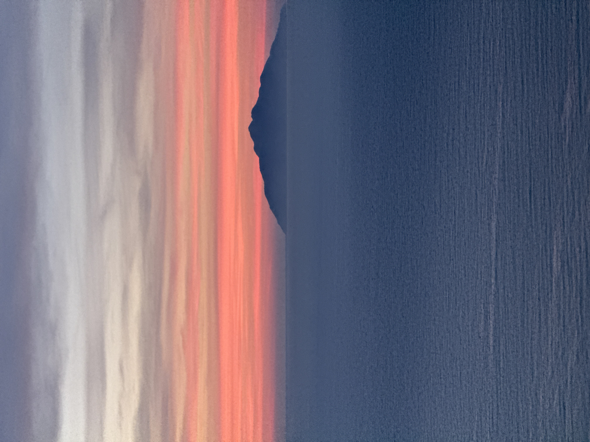 This image depicts a serene seascape at dusk, featuring a silhouette of an island against a gradient sky of soft pinks, oranges, and purples. The calm, deep blue ocean fills the foreground and middle ground. The horizon line is clearly defined by the meeting of the sea and the sky. There are no people or specific urban elements visible, suggesting a natural landscape rather than a cityscape. The absence of distinct landmarks or recognizable structures means the location cannot be identified as Đà Nẵng, Vietnam, or any other specific city.