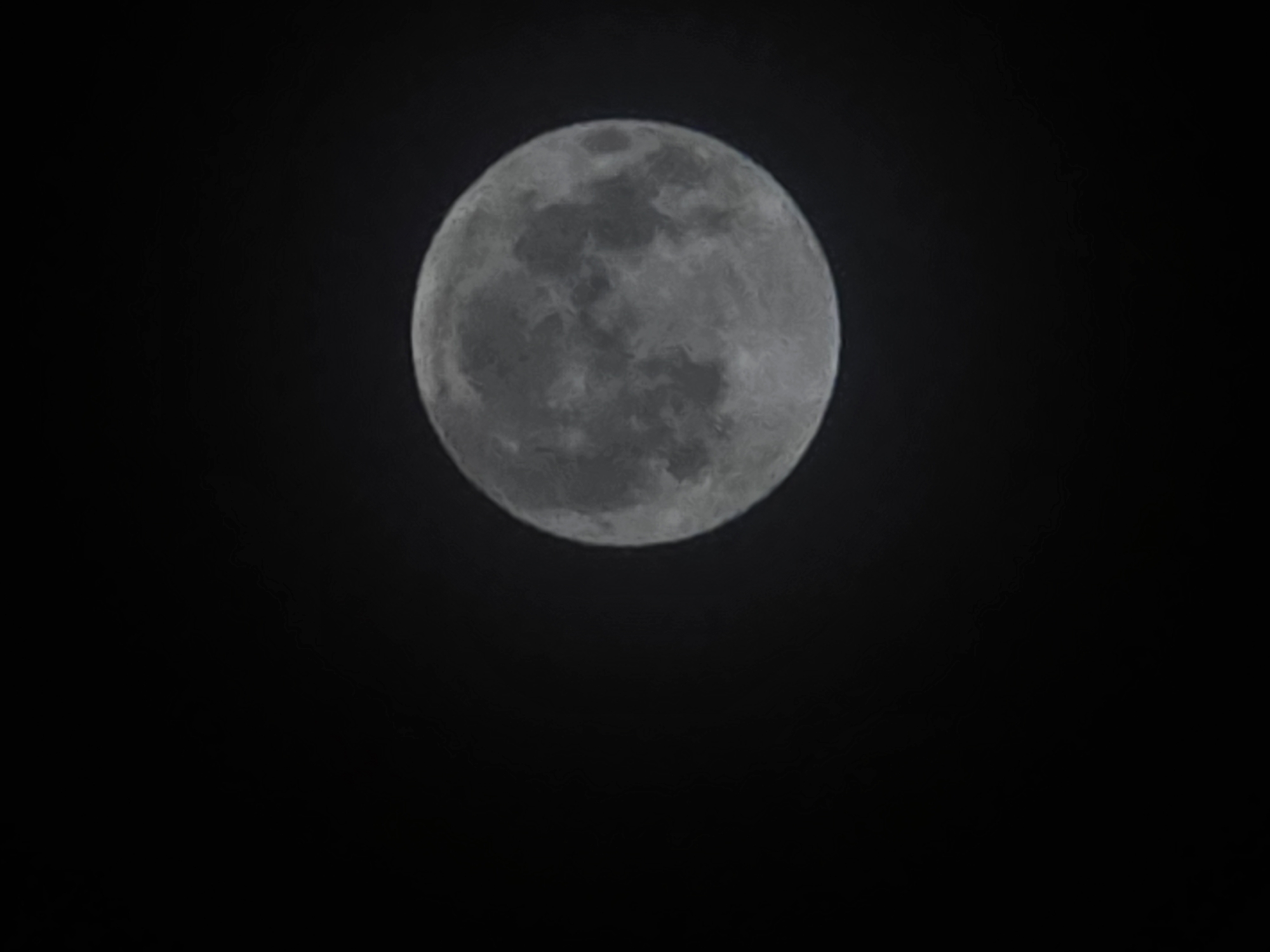 The image displays a full moon against a dark night sky. The moon is the central subject, occupying the right half of the frame, and its surface details, including craters and maria, are visible. The rest of the image is pure black, suggesting a clear night with no visible stars or atmospheric haze. There are no man-made structures or identifiable geographical features visible in the image. The image does not provide any context or information to determine its location in Salzburg, Austria, or any other city.