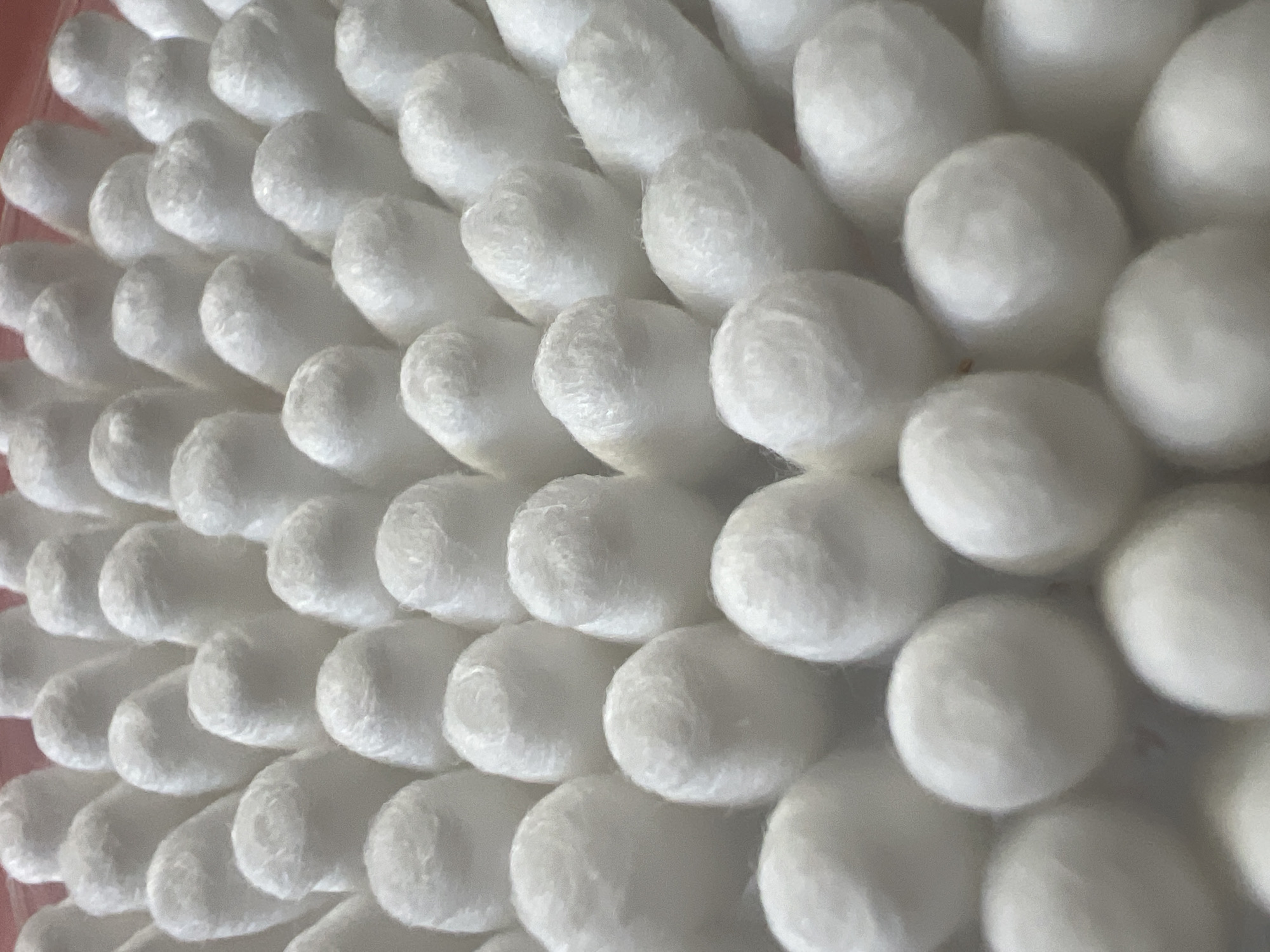 The image shows a close-up, overhead view of a large group of white cotton swabs arranged in a pattern. The swabs have fluffy, rounded tips and appear to be packed tightly together. The lighting is soft and diffused, creating gentle shadows. There is no indication of location in Pskov, Russia. The scene is static and contains only the cotton swabs.