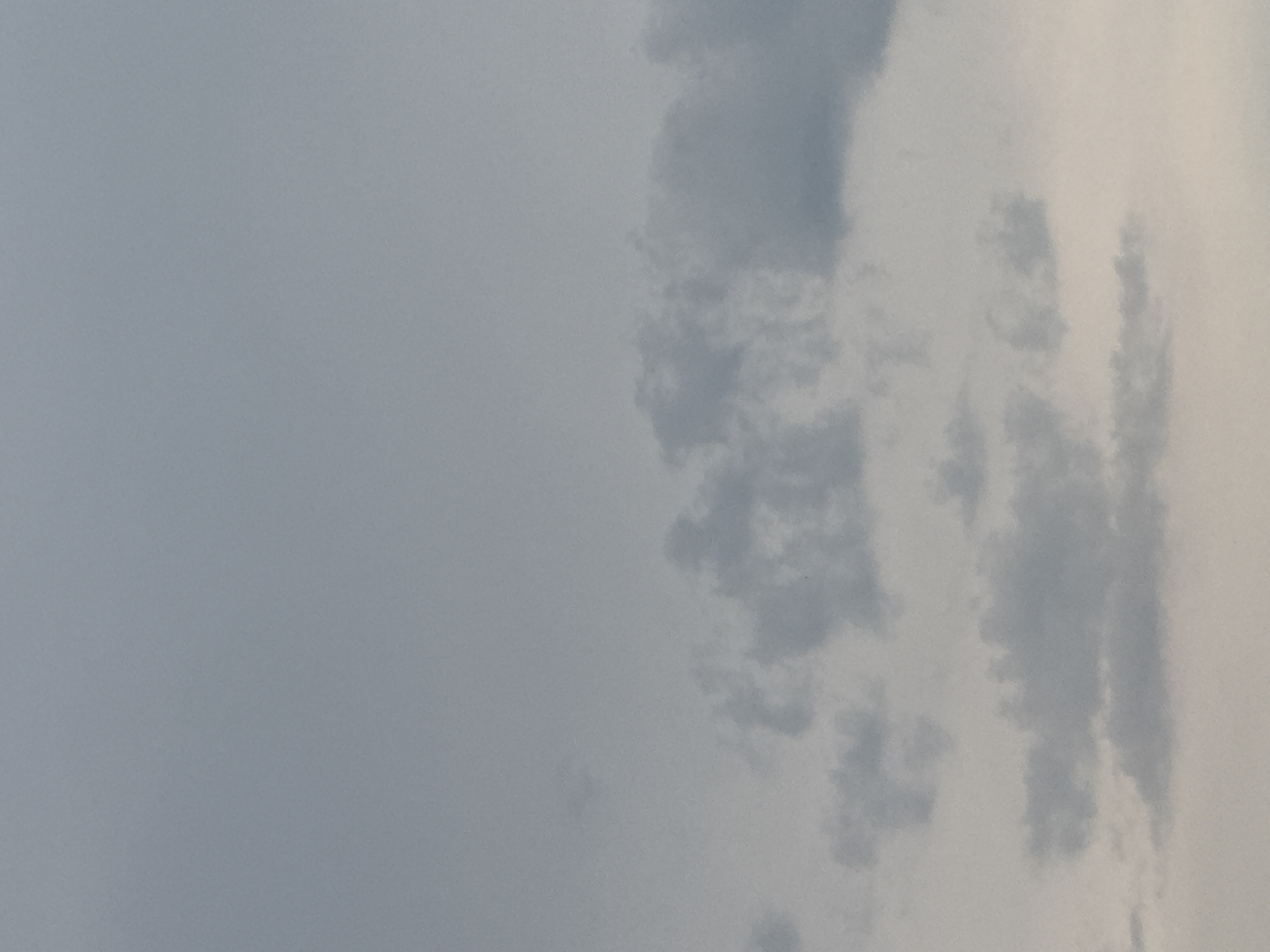 The image shows a cloudy sky with shades of gray and white. The clouds are scattered and appear to be low-lying, obscuring a clear view of the horizon. The lighting suggests it might be overcast or nearing sunset. The image does not contain any identifiable landmarks or features that would indicate a specific location within Tbilisi, Georgia. There are no people, subjects, objects, or actions visible in the scene. The environment is entirely composed of the sky and clouds.