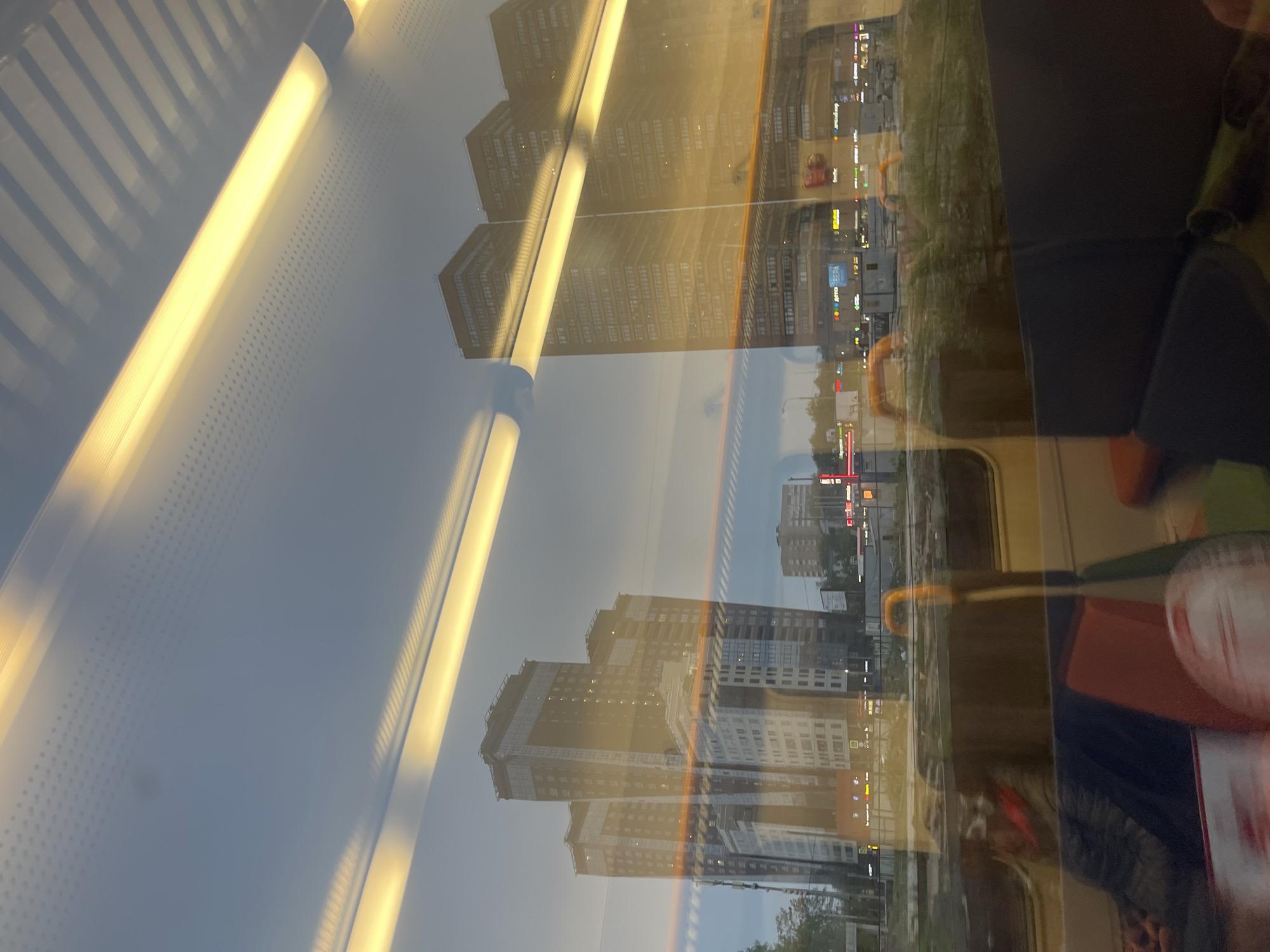 The image, taken from inside a train or bus, shows a reflection of buildings and city lights on the window. The interior of the vehicle includes seats and fluorescent lights. The reflection indicates that the location outside is the city of Khimki, Russia. The tall buildings are reflected along with the signage and street lights of the city.