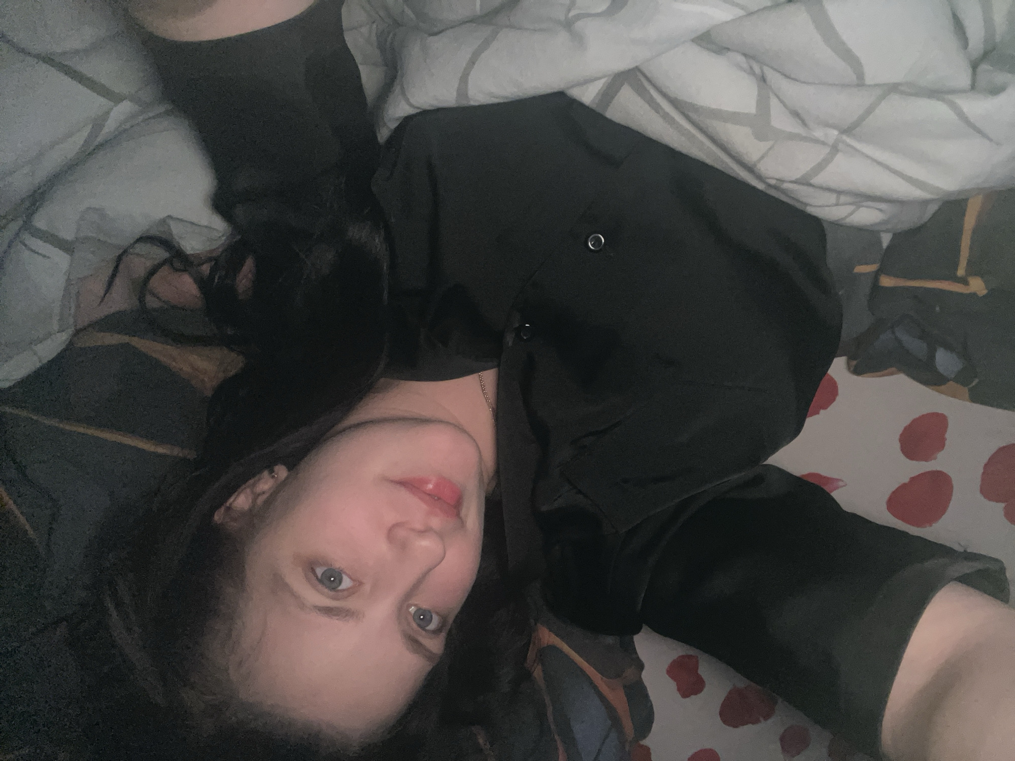 A woman with dark hair and light eyes is lying on a bed. She is wearing a black shirt. The bed has patterned sheets and a grey and white blanket. The location is not discernible as Марковский, Russia based on the image.