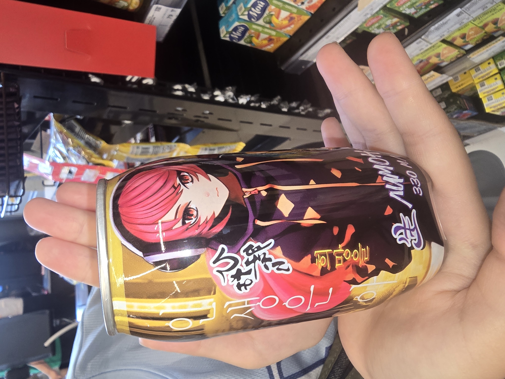 The image shows a close-up of a hand holding a can of an energy drink. The can features an anime-style illustration of a person with pink hair wearing headphones and a hoodie. The background appears to be a retail environment, likely a convenience store or supermarket, with shelves stocked with various products, including juice boxes. The lighting suggests an indoor setting. The location of Ulan-Ude, Russia is not discernible from the image itself; this information is external to the visual content.
