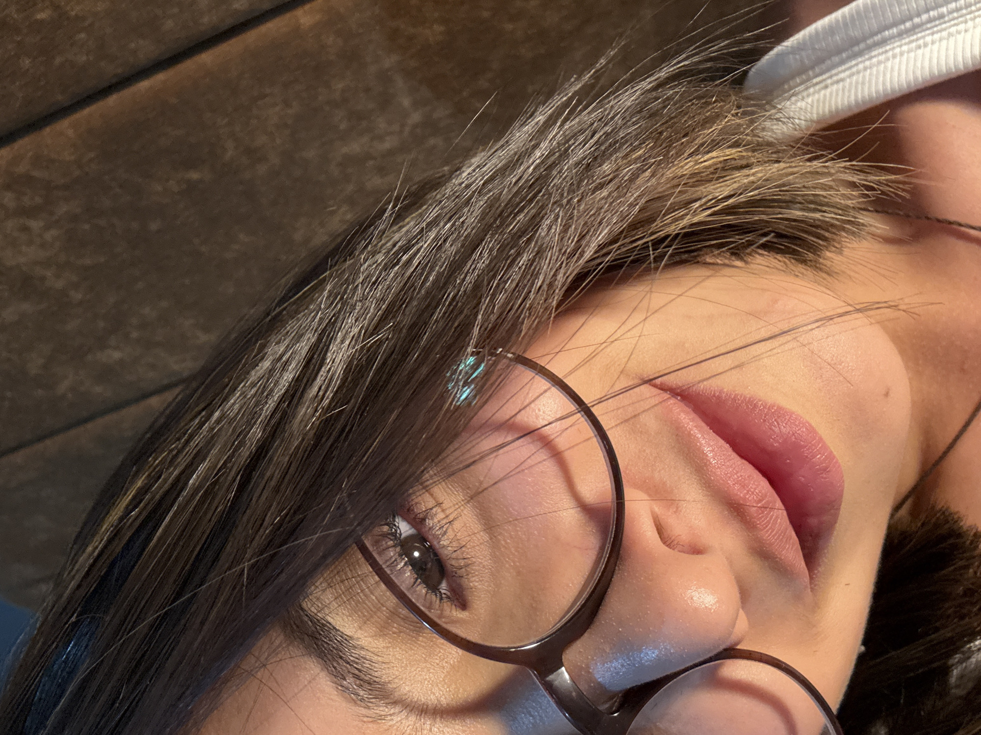A close-up, upward-angled shot focuses on a woman's face. She is wearing glasses with a brown frame, and her eye is visible behind the lens. Her hair is dark brown and partially covers her face. Her lips are a light pink color. The background appears to be wooden. The image does not provide any information to suggest that the image was taken in Puebla, Mexico.