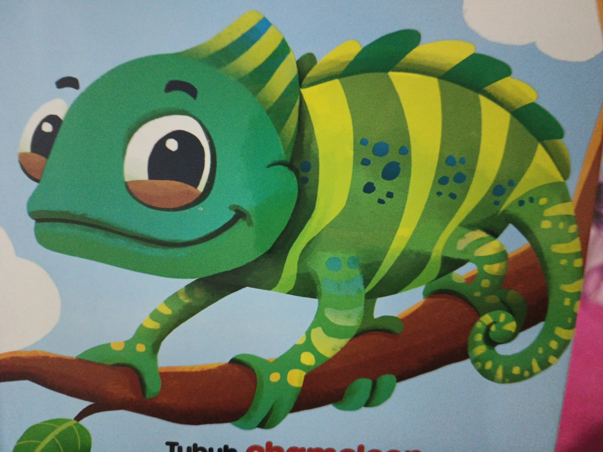 A cartoon chameleon is depicted in a vibrant green and yellow color scheme, perched on a brown branch against a light blue background. The chameleon has large, expressive eyes with black pupils and white sclera, framed by brown eyelids. Its head features a crest with yellow and blue stripes. The chameleon's body is adorned with alternating green and yellow stripes, and smaller blue and yellow spots. It has distinct feet, with two on the branch and others visible as it grips the limb. A single green leaf is positioned below the branch. The image appears to be a page from a children's book, as indicated by the text "Tubuh chameleon" (meaning "Body of a chameleon") partially visible at the bottom. The overall style is playful and illustrative. The location of this image in South Jakarta, Indonesia, cannot be determined from the visual information provided.