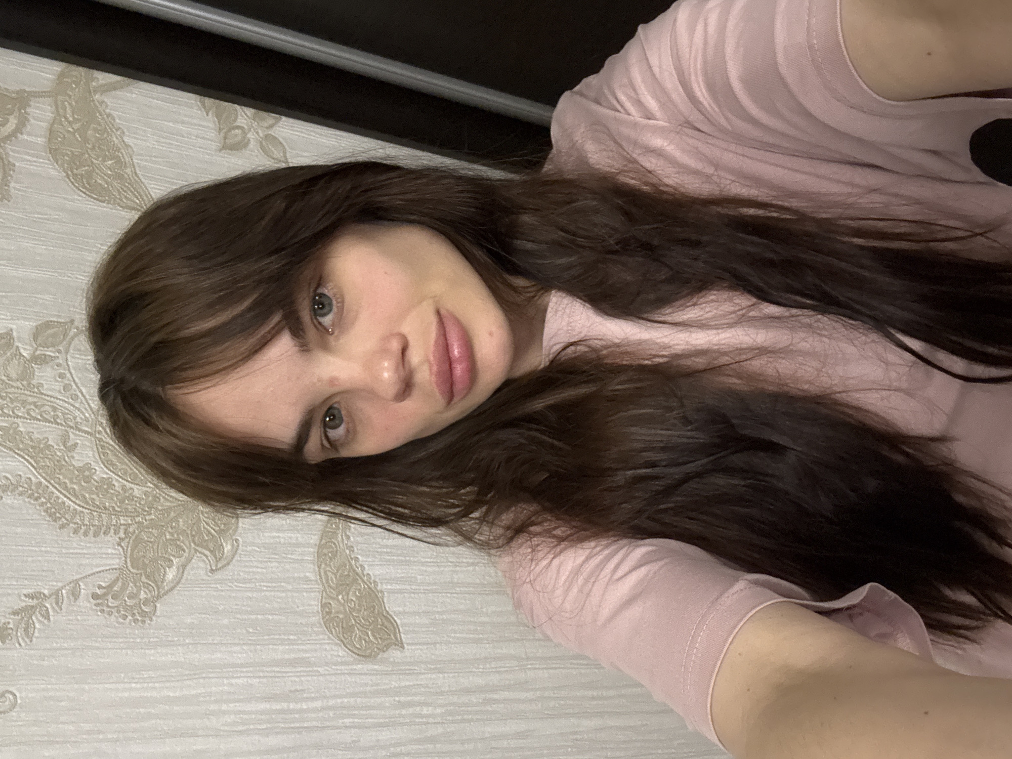 A woman with long brown hair and blue eyes lies on a surface with patterned wallpaper. She is wearing a light pink shirt. The location in Rostov-on-Don, Russia, is not discernible from the image.