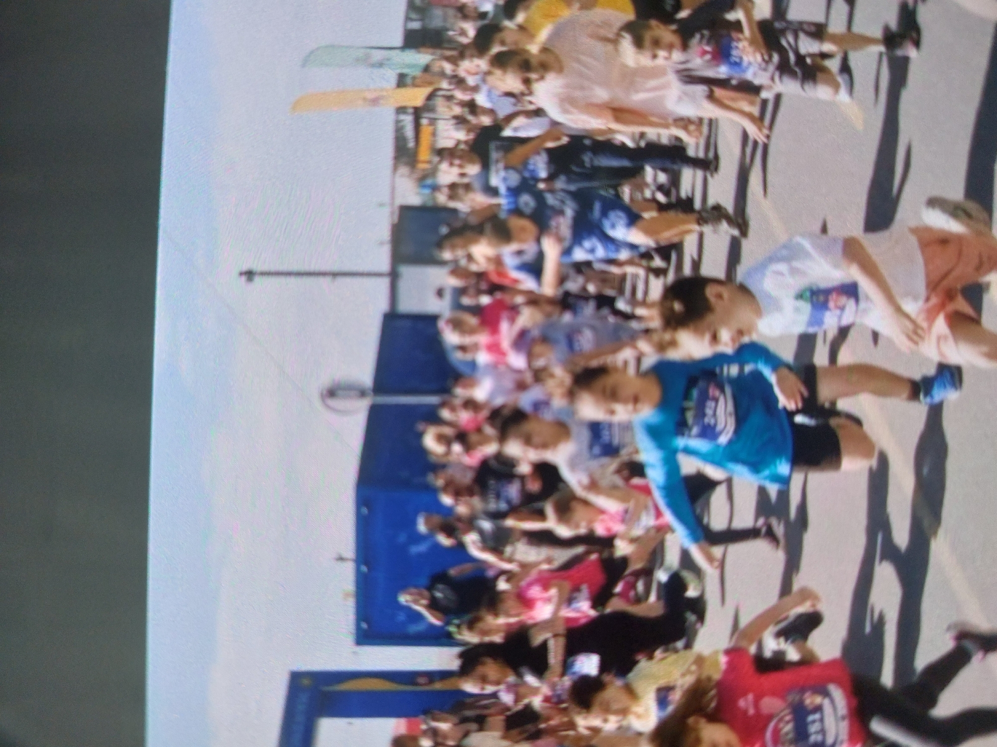 A crowded outdoor scene in Tsarevo, Bulgaria depicts participants near the starting line of a running event. Many individuals wear running attire and bibs with numbers on them. A blue inflatable archway marks the starting point. Banners, flags and signage adorn the area. The weather appears sunny.