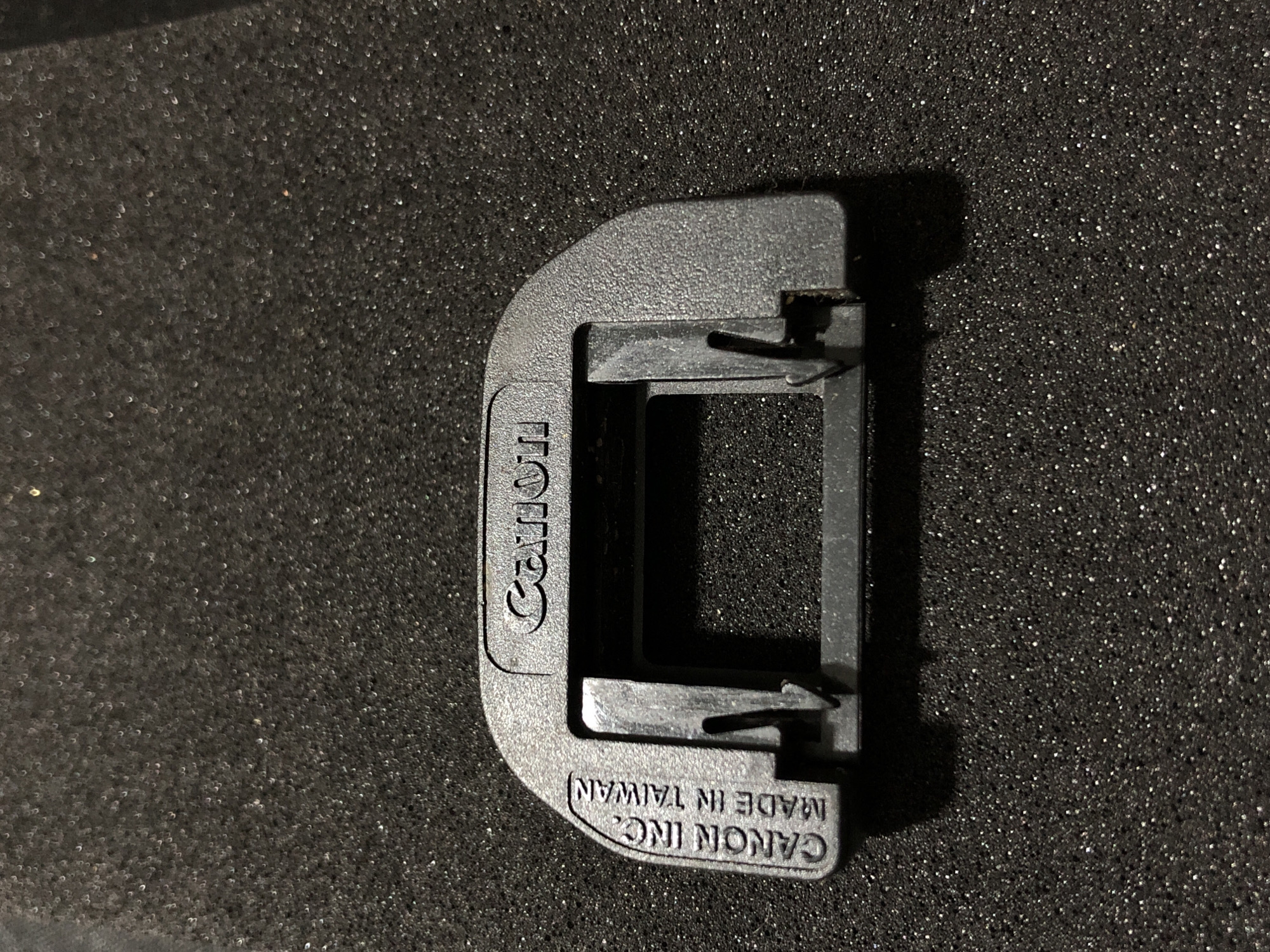 A black, plastic Canon brand eyecup for a camera is shown lying on a textured black surface. The eyecup has "CANON INC. MADE IN TAIWAN" embossed on the left side and "Canon" embossed on the right side. The image does not provide any information about the city of Yelizovo, Russia, or any other geographical location.