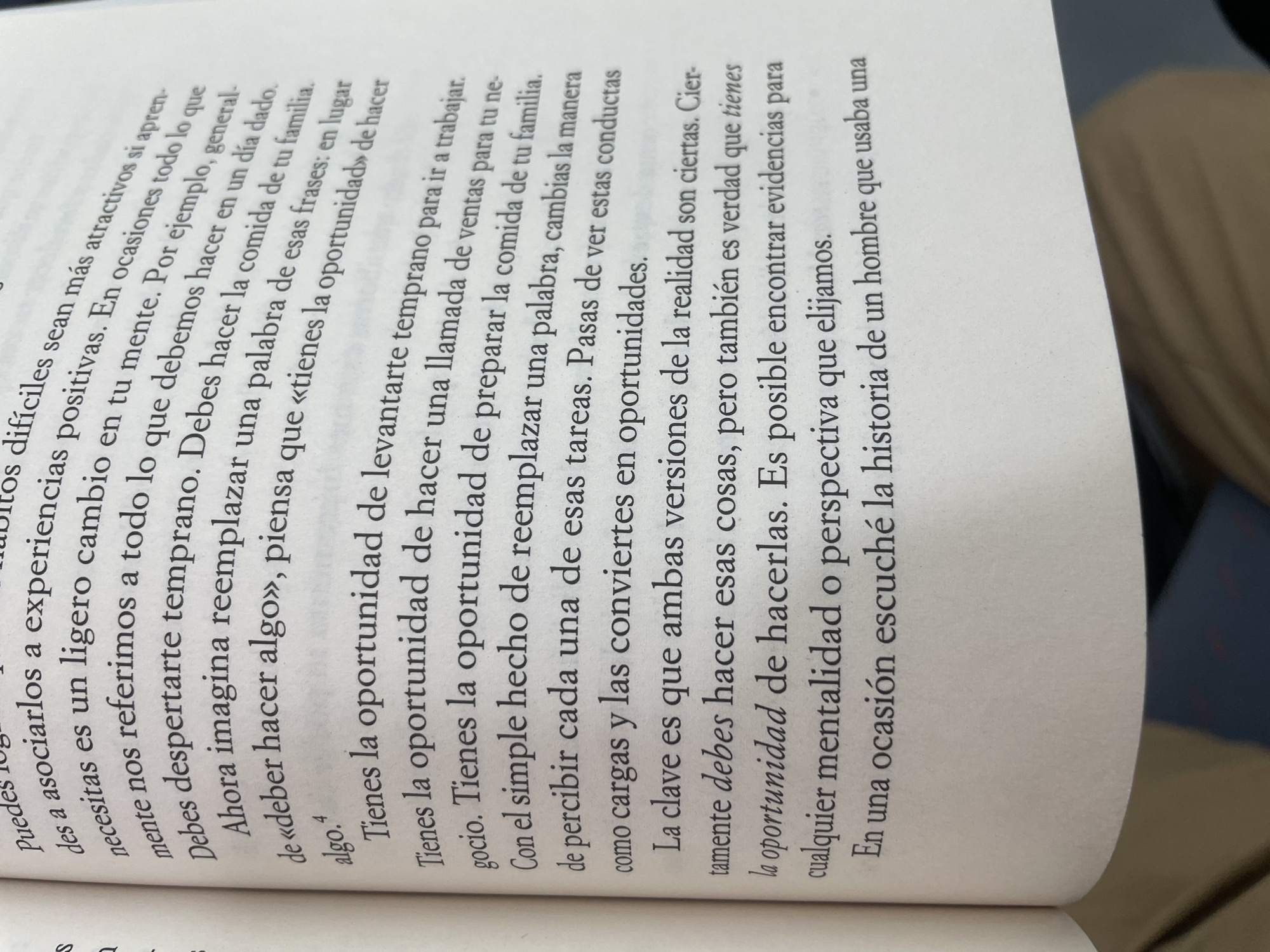 Here's a detailed description of the image:
**Scene:** A close-up shot of a book open to a page of Spanish text. The book appears to be lying on a surface, and part of someone's clothing (likely pants) is visible in the background, suggesting the book is in a casual setting.
**Text Content:** The Spanish text on the page seems to be from a self-help or motivational book. The text discusses changing one's mindset to view obligations as opportunities. Key phrases include: "oportunidad" (opportunity), and a discussion of replacing phrases like "deber hacer algo" ("must do something") with "tienes la oportunidad" ("you have the opportunity"). The final line mentions a story the author once heard about a man.
**Overall Impression:** The image gives the impression of someone reading or studying the book. The focus is on the content of the text, suggesting the importance of the message being conveyed.
**Location in Sant Adrià De Besòs, Spain:** While it is not possible to determine the exact location of the image, I can affirm that the location is not within Sant Adrià De Besòs, Spain. The image is of a book, not a location.