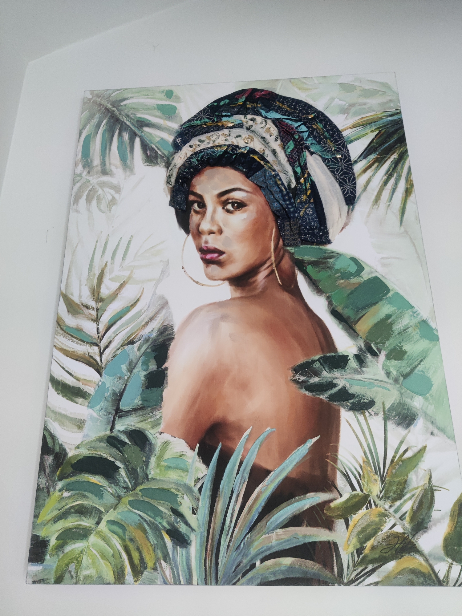 A painting of a woman wearing a headwrap and large hoop earrings is displayed on a white wall. The woman is shown from the shoulders up, with her back turned to the viewer. She is surrounded by lush green foliage, with large tropical leaves framing her. The style of the painting is impressionistic, with visible brushstrokes and vibrant colors. There is no indication of a specific location within Katerini Municipality, Greece.