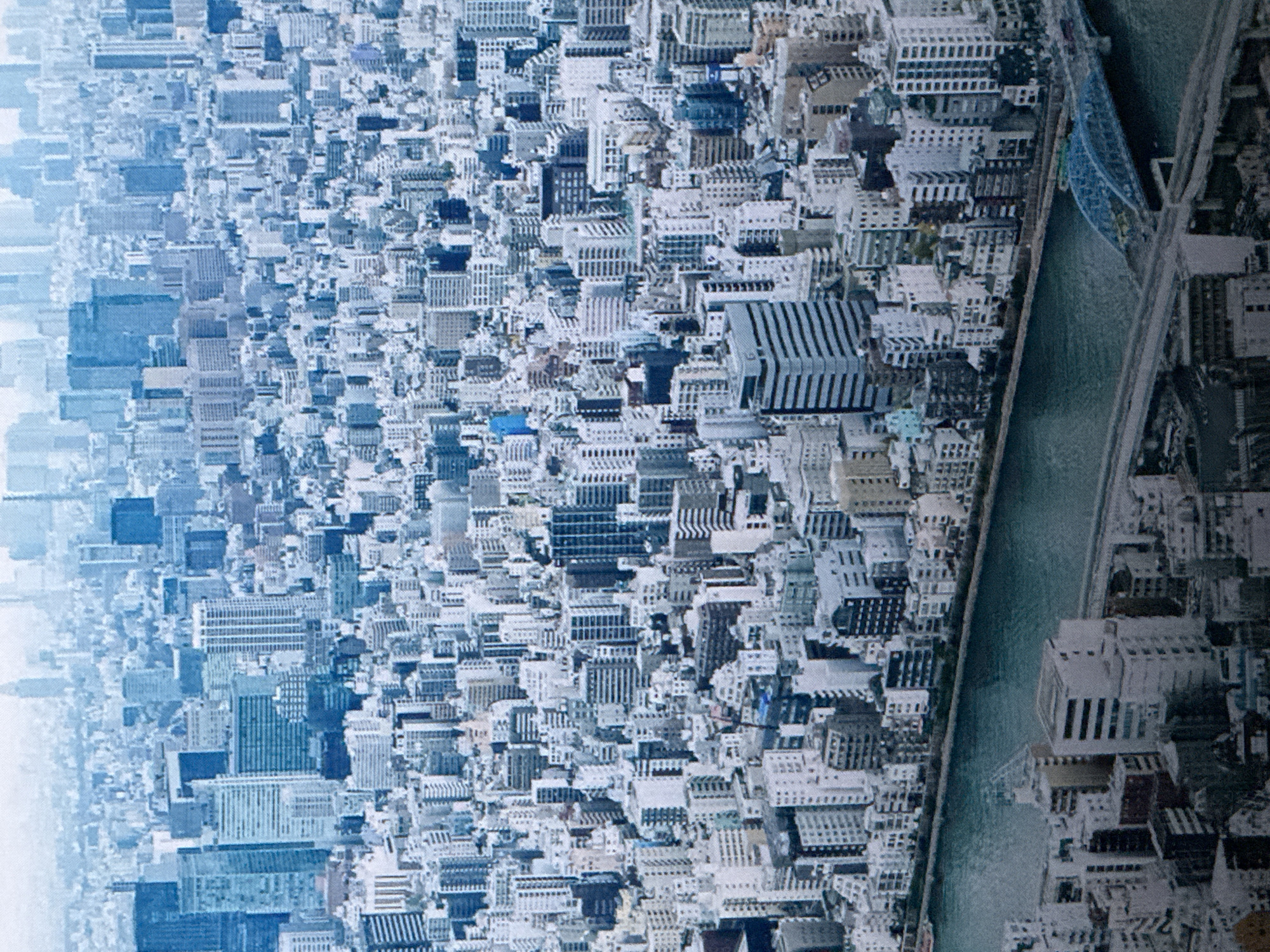 This is an aerial, high-angle, daylight, wide shot of a densely packed urban environment, dominated by a vast expanse of buildings. The architecture consists of numerous high-rise structures, ranging from the mid-rise to skyscrapers, predominantly rendered in shades of white, light gray, and dark blue. A body of water, appearing as a river or large canal, runs through the lower portion of the frame, crossed by at least two bridges, one of which is a distinctive blue arched structure. The city stretches to the horizon, where it fades into a hazy, bright sky, suggesting a large metropolis. The overall impression is one of extensive development and urban density. The location is identified as Saratov, Russia. There are no visible people or specific actions being depicted.