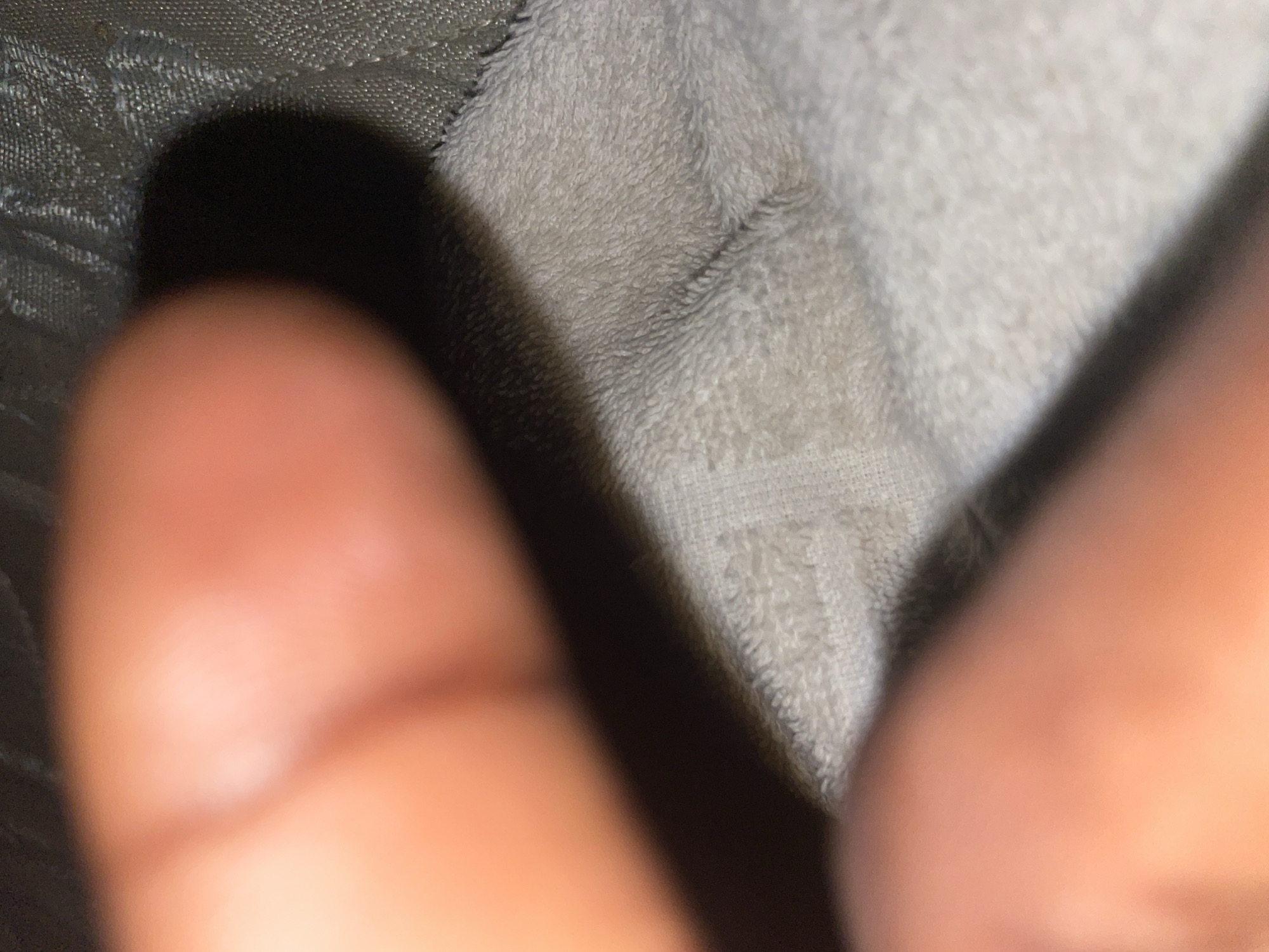 The media file is a close-up, out-of-focus photograph featuring a person's fingers in the foreground, casting a shadow on a textured surface. The background consists of two distinct materials: a dark, woven material on the left and a lighter, fluffy textile on the right. The lighting suggests an indoor setting, as a strong shadow is cast by the fingers, indicating a direct light source. The overall impression is one of informality, possibly a candid shot or an accidental capture. No text is visible in the image. The provided location context of Ilorin, Nigeria, does not offer specific visual cues within the image itself.