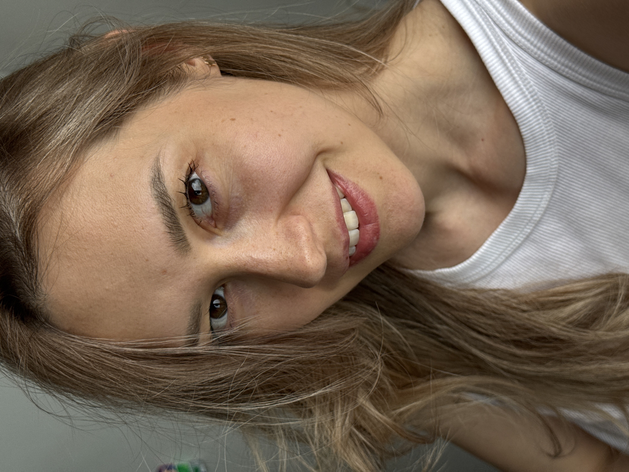 A close-up portrait shows a woman with light brown hair, brown eyes, and a slight smile. She is wearing a white tank top. The image is rotated. There is no evidence to indicate that the image was taken in Chaikovsky, Russia.