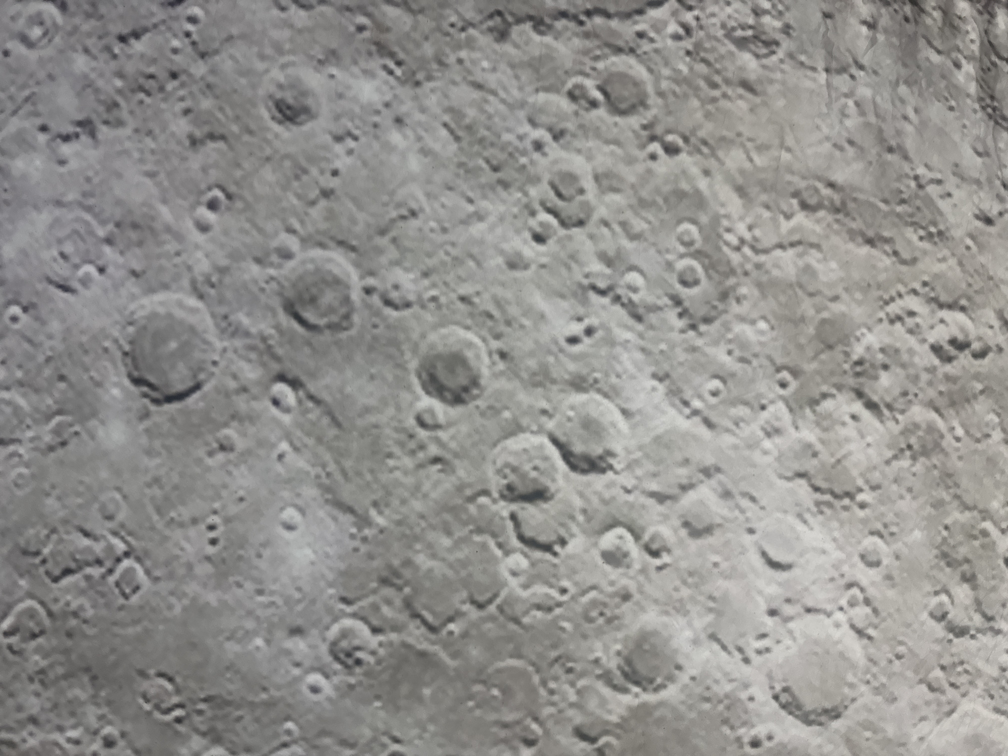 The image is a close-up, high-angle view of the surface of the Moon, showing numerous impact craters of varying sizes. The surface appears predominantly gray and textured, with shadows cast by the rims of the craters, indicating oblique lighting. There are no people, man-made objects, or any signs of life visible in the image. The environment is extraterrestrial and barren.
It is not possible to determine the location within the city of Baan Pang Ka, Thailand, as the image depicts the surface of the Moon.