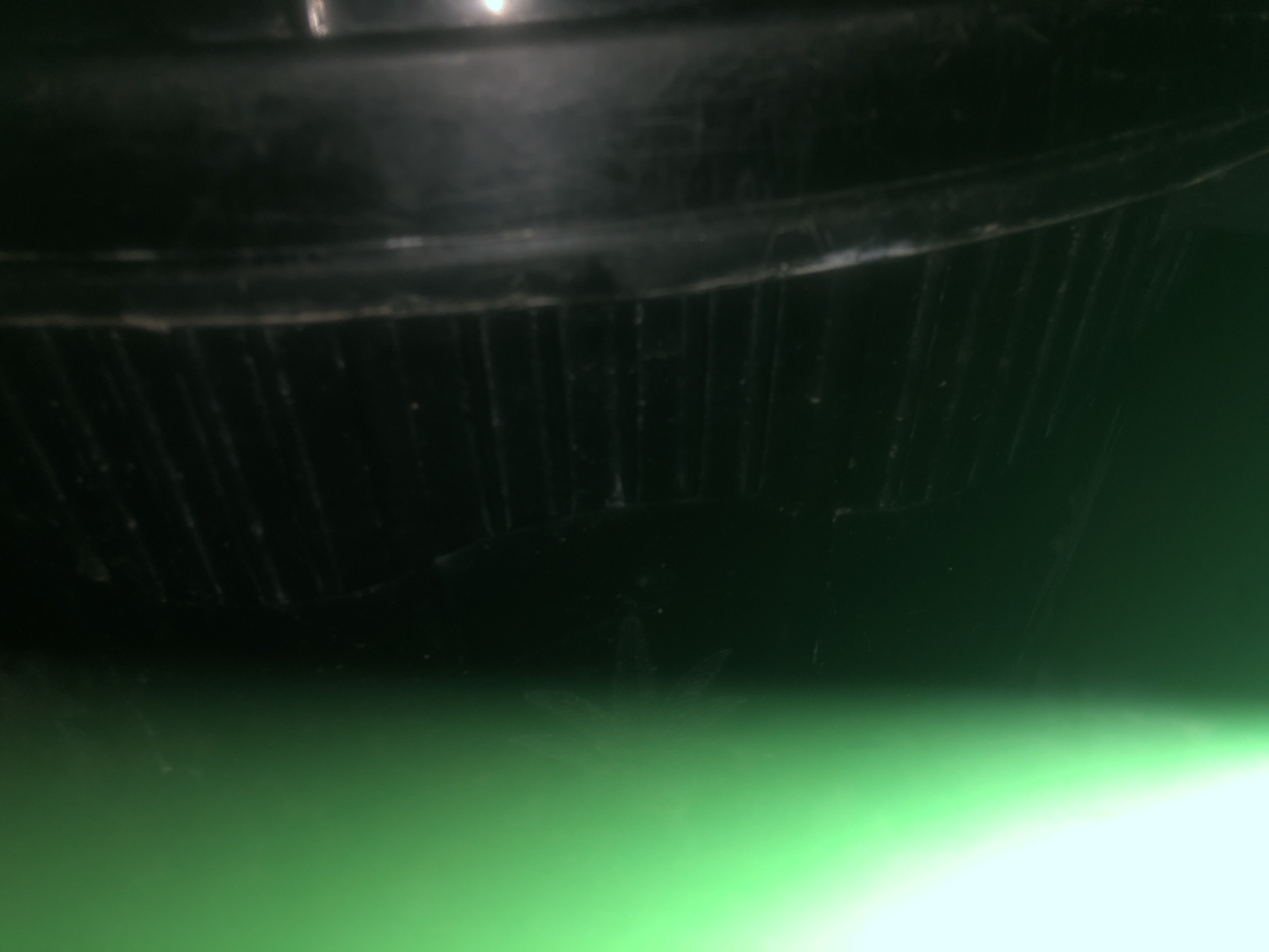The image displays a close-up view of a dark-colored object with vertical ridges. The object appears to be made of plastic and has a textured surface. The lower portion of the image transitions into a bright green hue, suggesting it is either a brightly lit background or a surface with a strong green color. The overall lighting is dim, with some reflections visible on the object's surface. There are no people or identifiable landmarks present in the image. The location in Jalingo, Nigeria cannot be determined from this image.