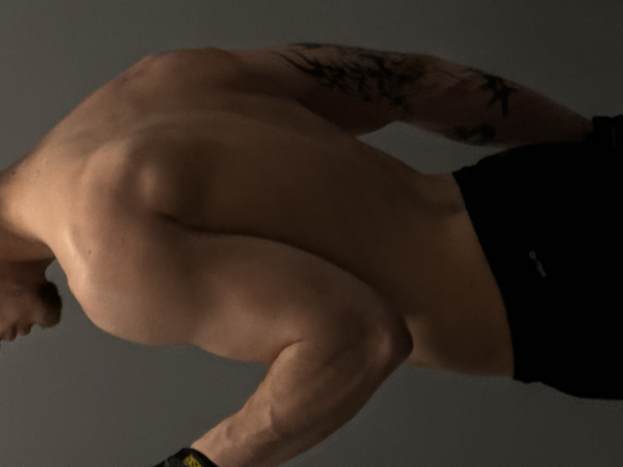 A bare-chested man with tattoos on his arm is wearing black shorts. He is indoors. There is no evidence to indicate the location is Sofia, Bulgaria.
