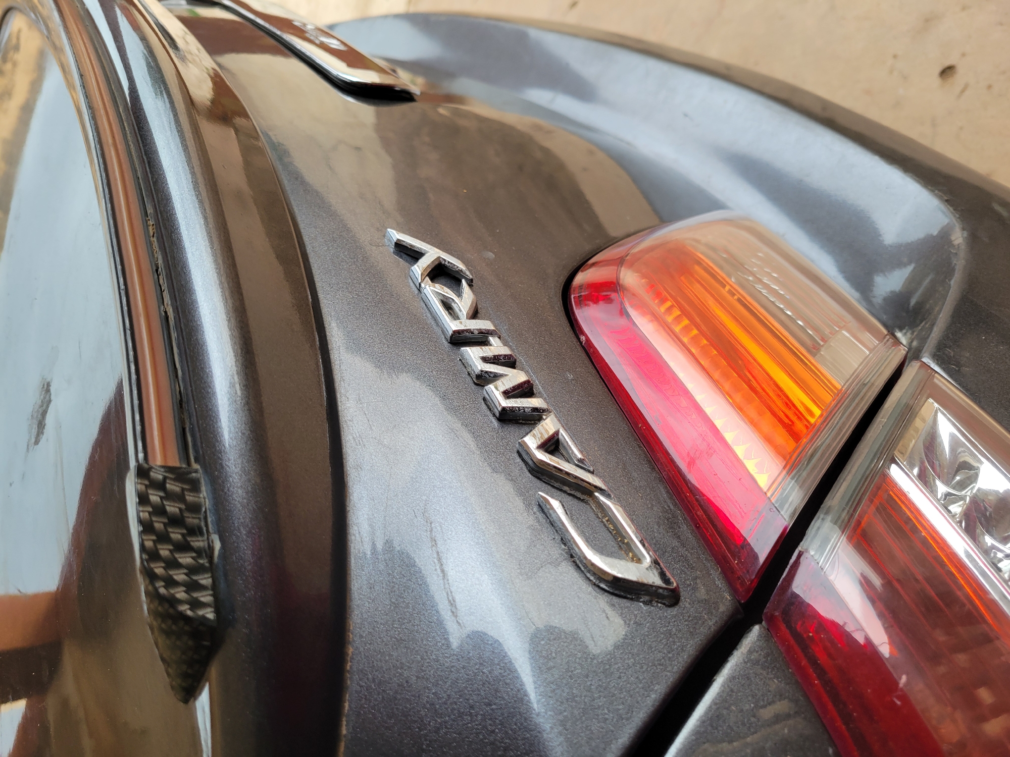 A close-up shot of a dark gray car trunk with a "RWD" emblem. The trunk also has the car's taillight on the right. The car is in an unknown location.