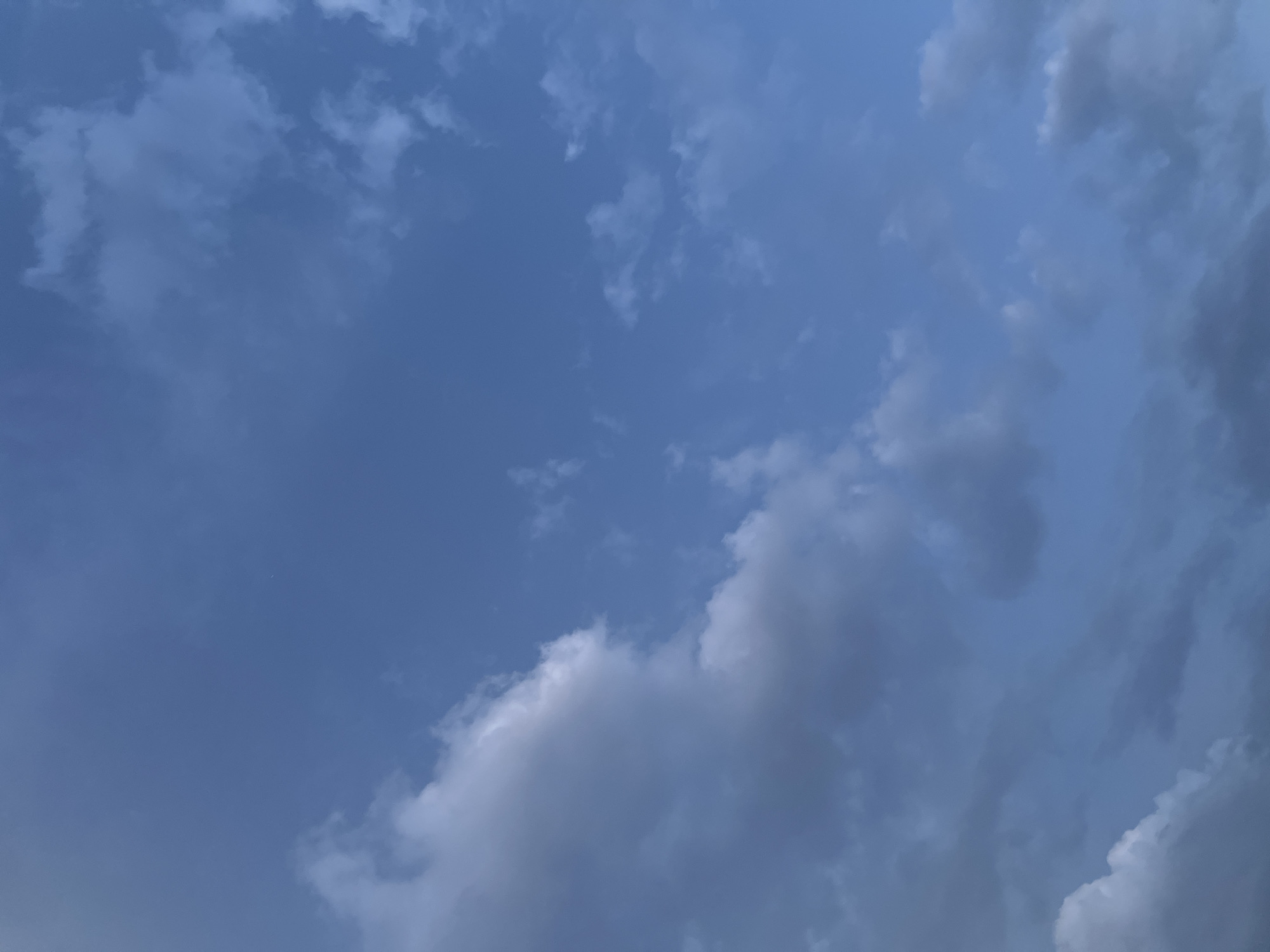 The image depicts a sky filled with clouds, with a prominent large cloud formation on the left side, appearing white and gray. The rest of the sky is a blue hue, with scattered smaller clouds of varying gray tones. The lighting suggests it might be late afternoon or early evening. There are no people, structures, or any recognizable landmarks of Krasnoyarsk, Russia, visible in the image. The scene is purely a natural sky scape.