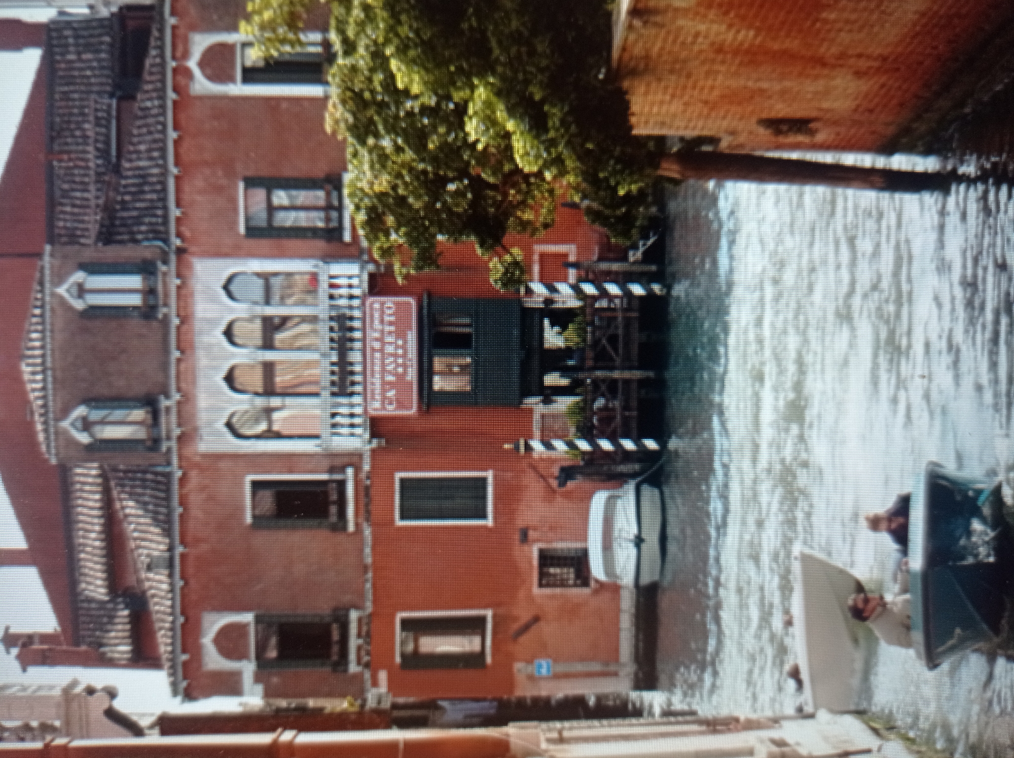 The image depicts a canal in Venice, Italy, with a traditional Venetian building on the right. The building is painted in a terracotta color and features arched windows and ornate balconies. A sign is visible on the building, reading "Residence D'Epoca CA FAVRETTO". Trees and vegetation partially obscure the building.
In the foreground, a canal is filled with water, reflecting the sky and the buildings. Two small boats are present in the canal. One boat, a dark-colored vessel, is in the immediate foreground, carrying two individuals. The person in the front is wearing sunglasses and a light-colored jacket, while the person behind them is wearing dark clothing. Behind this boat, a white boat is partially visible, docked or moving slowly.
The overall scene is characteristic of the picturesque canals of Venice, with its historic architecture, waterways, and boats. The image does not show any elements related to Mukachevo, Ukraine.
