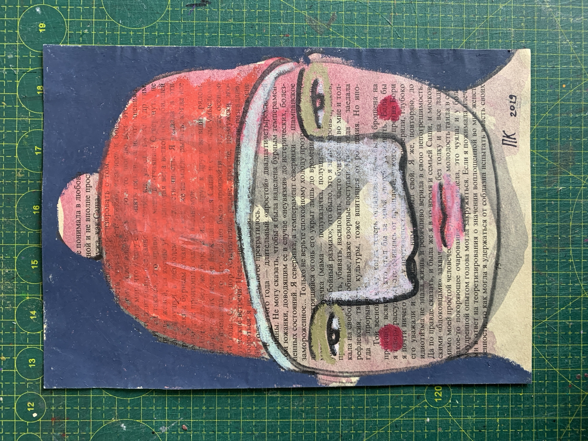 The image is a mixed-media collage depicting a stylized portrait of a person. The portrait is rendered on a background of text from a book, with visible grid lines from a cutting mat. The face is painted in a muted palette with broad strokes, featuring prominent eyes with dark irises and green accents around them, and a red hat that covers the top of the head. The body of the person is suggested by the shoulders, also painted over the text. The text itself is in Russian and contains various handwritten notations and dates, including "120" and "75" on the left and bottom edges respectively. The bottom right corner has a signature or initials "ПК" and the year "2019". There are no discernible elements that indicate a specific location within Sergeevo, Russia.