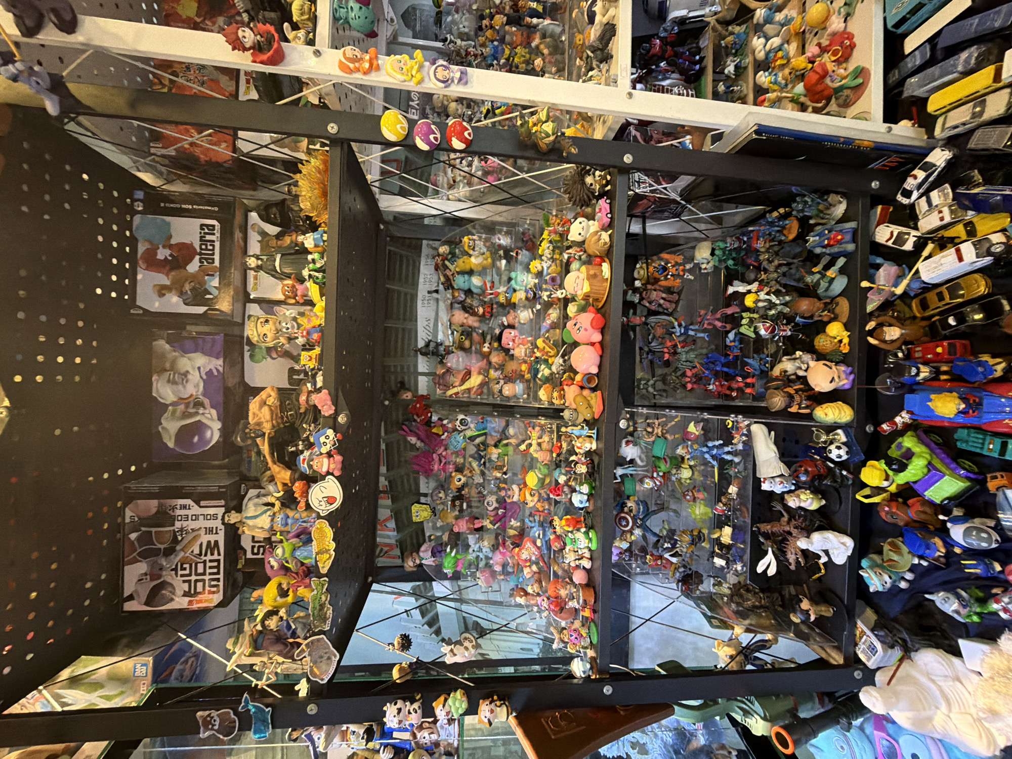 The image shows a large, multi-shelf display filled with a vast collection of anime figurines, toys, and collectibles. The shelves are organized with numerous items densely packed together, creating a vibrant and visually rich scene. The collection includes a wide variety of characters and styles, suggesting a personal collection or a retail display.
The environment appears to be an indoor space, likely a shop or a dedicated hobby room, with lighting that highlights the colorful items. The display shelves are made of dark metal and appear to be part of a larger shelving unit.
While the image itself does not provide specific geographical markers, if this collection were located in Davao City, Philippines, it would likely be found in a specialty toy store, an anime merchandise shop, or potentially a private collection within a residence. Shops specializing in collectibles and anime goods are commonly found in commercial areas or malls in cities like Davao City.