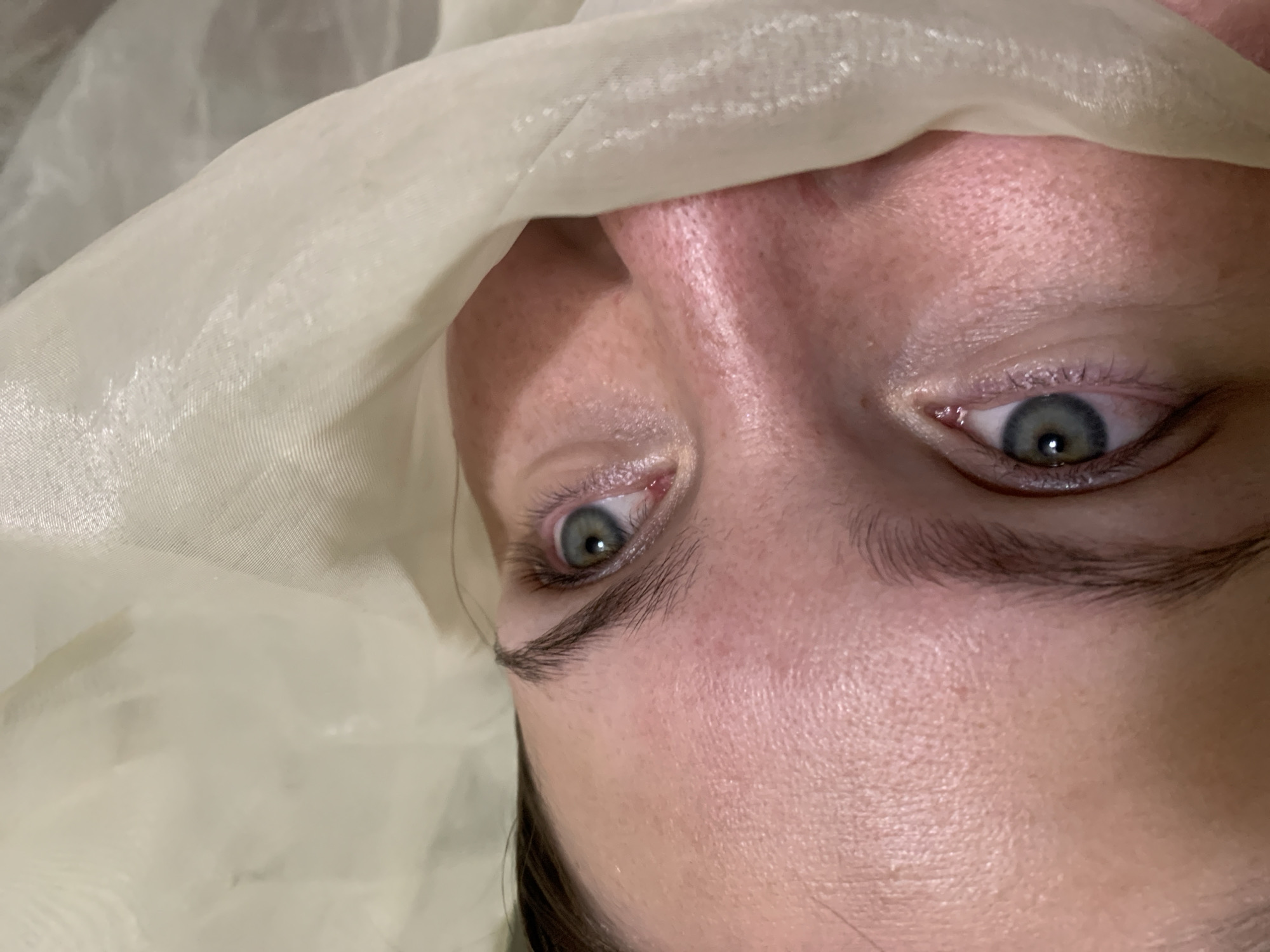 Close-up of a person's face with blue eyes, partially covered by a white, translucent cloth. Skin appears fair. The environment is nondescript, providing no indicators of location, specifically not revealing the city of Chaikovsky, Russia. No actions or interactions are visible.