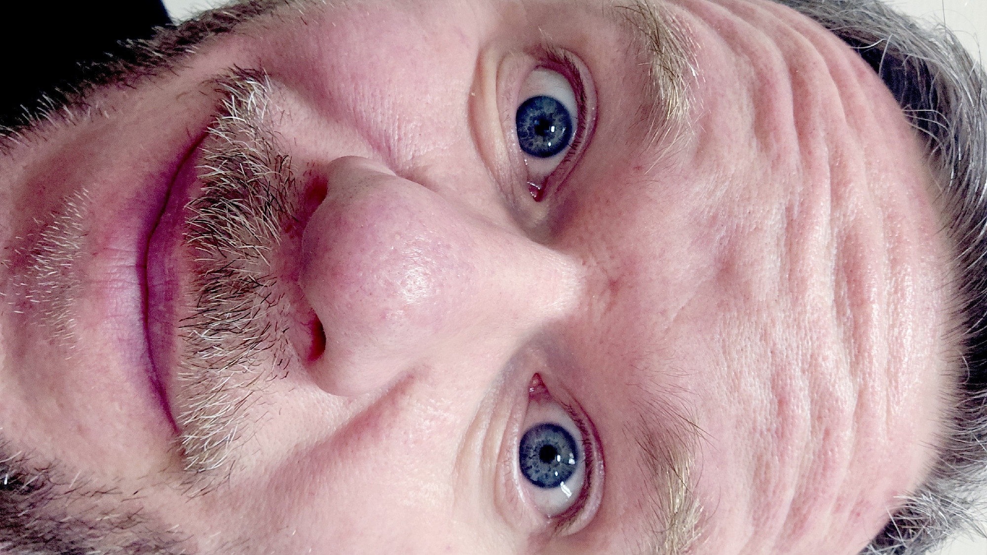 Close-up portrait of a man with blue eyes, a graying mustache, and forehead wrinkles. The image is oriented upside down. There are no indications of the location being Moscow, Russia, or any specific city.