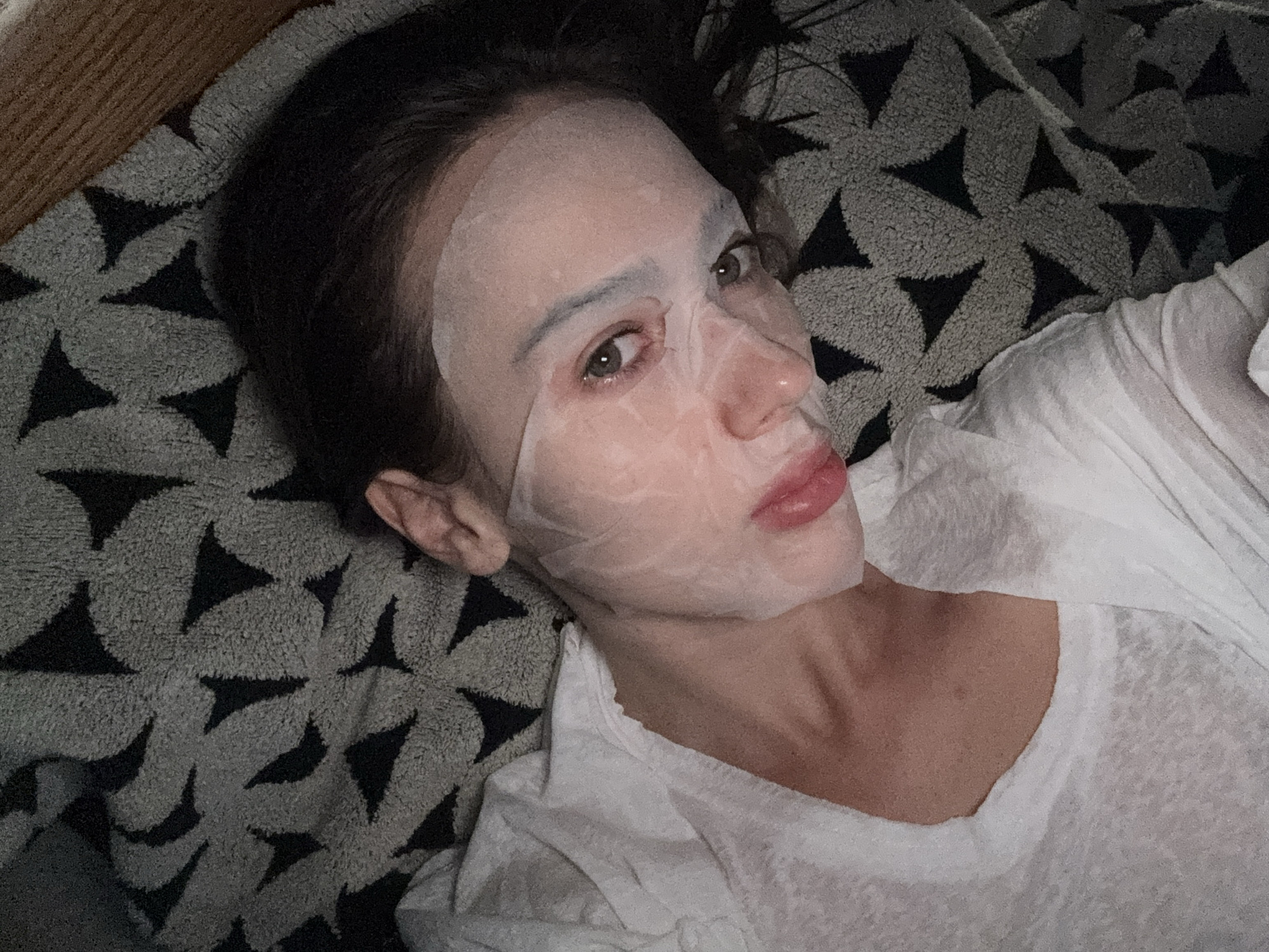 A fair-skinned woman lies on a black and grey patterned surface. She wears a white shirt and a facial mask. The location in Warsaw, Poland is unknown.