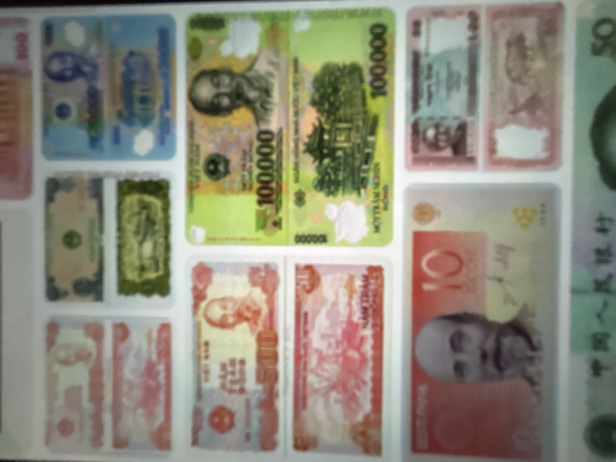 The image displays a collection of various international banknotes, arranged in a grid-like fashion. The banknotes are of different colors and denominations, featuring portraits of individuals, architectural scenes, and numerical values. Some banknotes are partially obscured by others or are out of focus, making precise identification challenging. There is no indication of the city of Gelendzhik, Russia, or any specific location within it. The scene appears to be a static display of currency, possibly for educational or collector purposes.