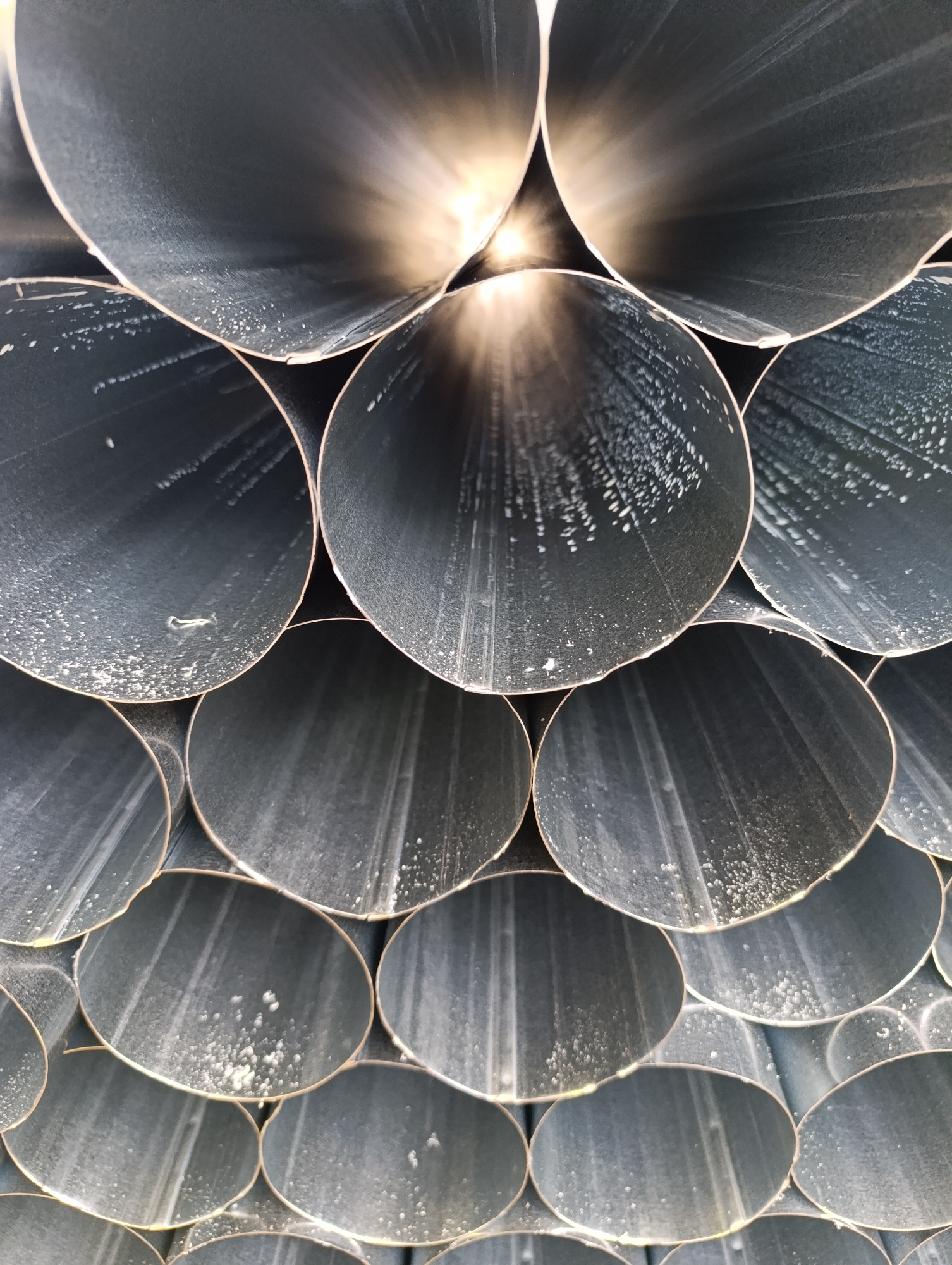 The image shows a stack of metal pipes with a gray, slightly textured surface. The pipes are arranged horizontally, with their circular openings visible. The interior of the pipes appears darker, with some light reflecting off the inner surfaces, creating a gradient effect. The overall impression is of a tightly packed, industrial arrangement of metal tubes. There is no evidence of the city of Haskovo, Bulgaria in the image.