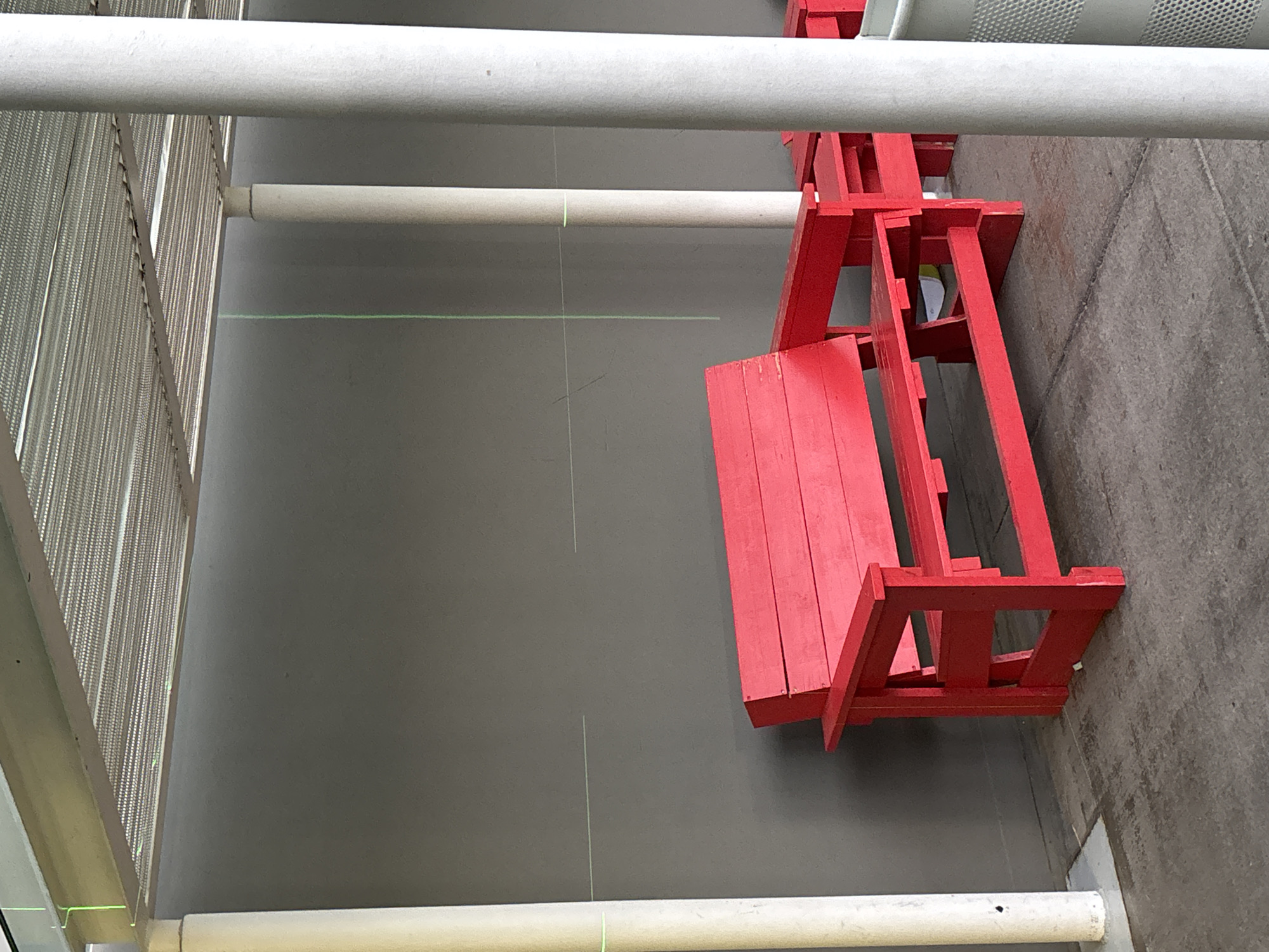 The image shows a red wooden structure resembling a bench or seating arrangement in a building, likely an art installation. The background consists of a gray wall or floor, with white cylindrical objects, possibly pipes or support structures, running across the scene horizontally. To the left, there's a metal mesh or grating structure. The image is captured from an elevated perspective.
While the scene seems to be indoors, there is no definite information to pinpoint the exact location in Mexico City. Therefore, the specific location cannot be confirmed based solely on this image.
