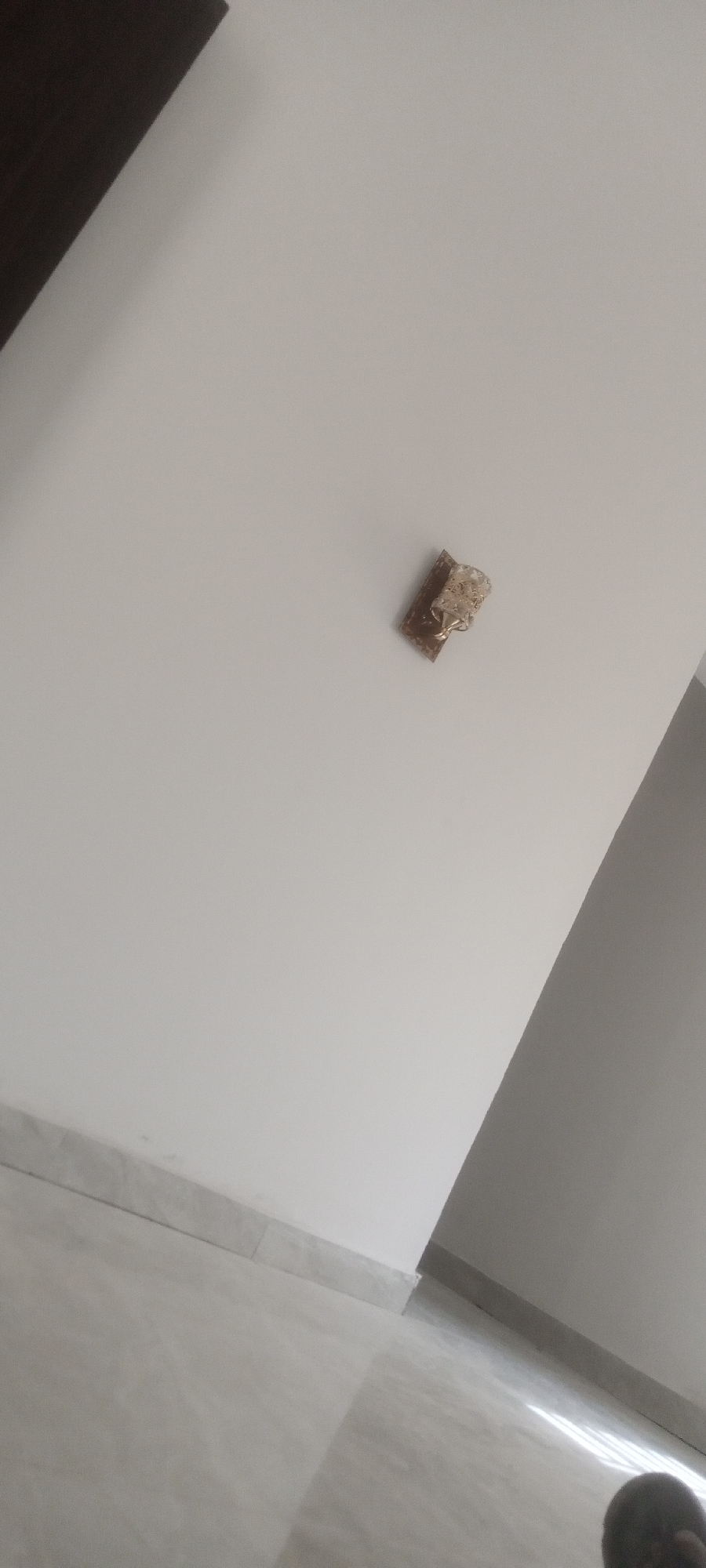 A damaged electrical outlet is visible on a white wall in an interior space. The outlet is missing its cover, exposing the wires. The floor is tiled. No people are visible in the main area. The scene is devoid of specific details indicating the exact location within Badiko, Nigeria.