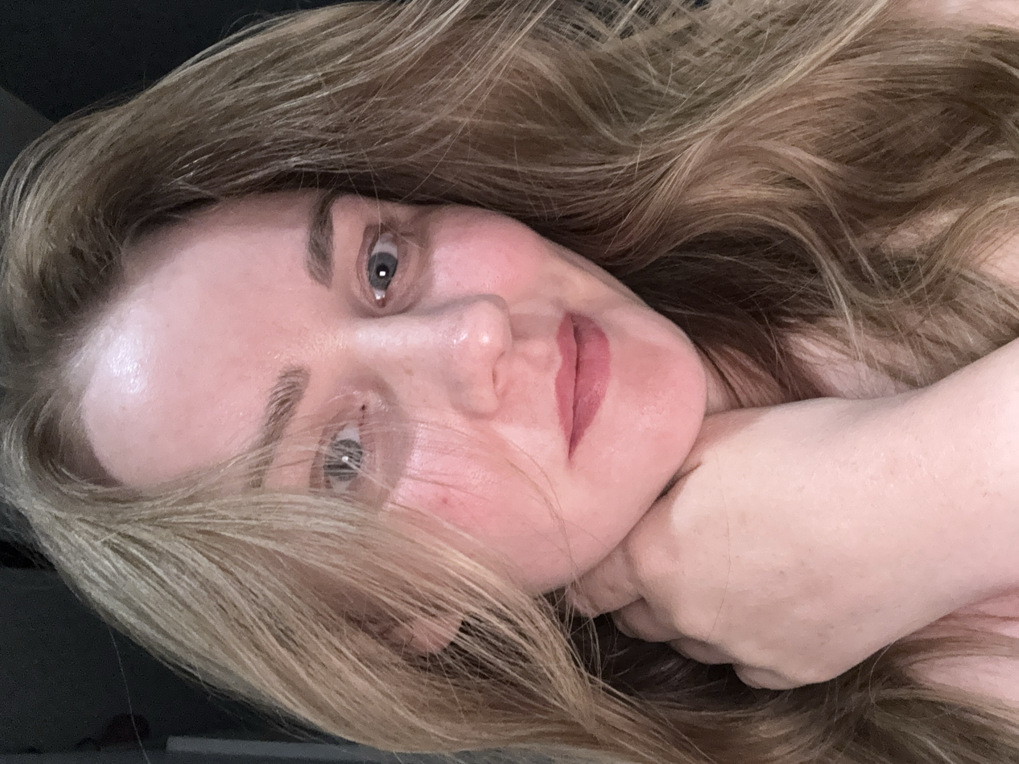 A close-up portrait of a woman with light brown hair and blue eyes is presented at an angle. The woman's face is slightly flushed, and her hand is positioned near her chin. The background appears to be dark, providing contrast to the subject's features. The absence of contextual cues prevents pinpointing the location to Chaikovsky, Russia, or any specific setting.