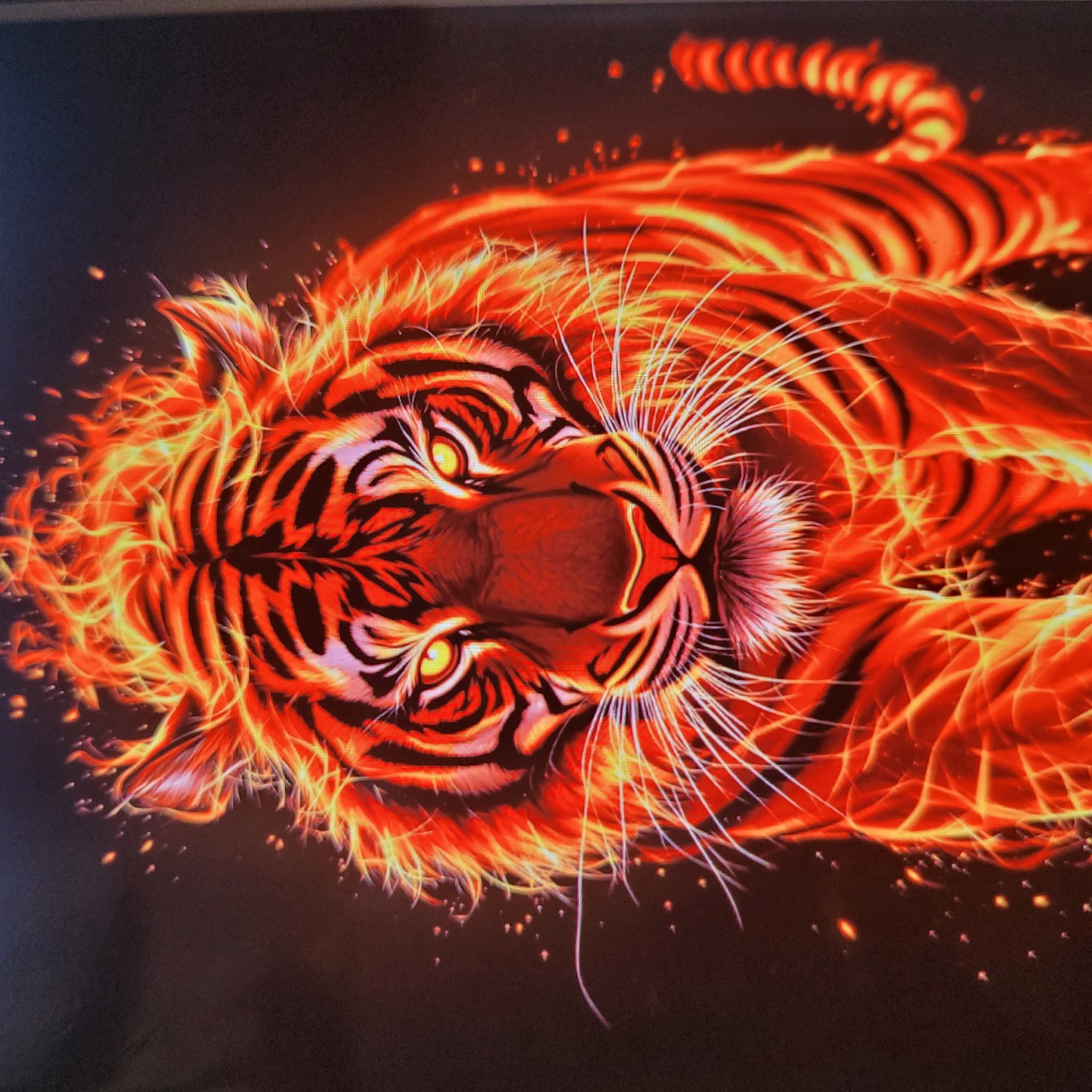 A highly stylized, digitally rendered image depicts a tiger composed of vibrant orange and yellow flames against a dark background. The tiger faces forward, with its eyes glowing yellow and its mane appearing as flickering flames. The fur is rendered with black stripes that are interspersed with fiery orange and yellow hues, creating an effect of the tiger being engulfed in fire. Small sparks and embers are scattered around the tiger, adding to the fiery aesthetic. The tiger's whiskers are depicted as thin, white, glowing lines. The overall impression is one of power and intensity. The image is a digital artwork and does not depict a real-world location.