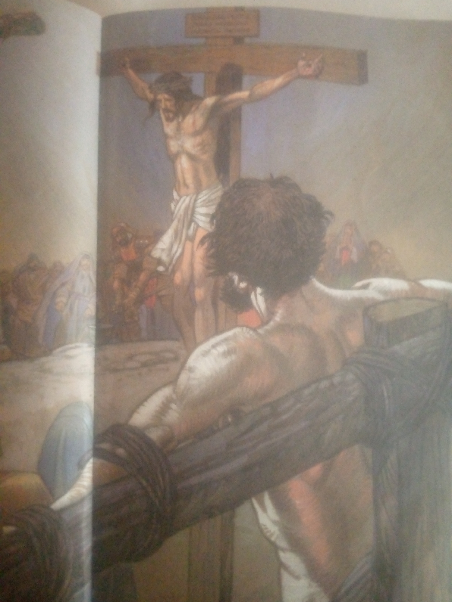The image depicts a painting of the crucifixion of Jesus Christ. In the foreground, a figure with dark, curly hair is seen from behind, with their arms wrapped around a wooden cross. This figure appears to be looking towards another, larger cross in the background. On the larger cross, Jesus is depicted with a loincloth and a crown of thorns, his arms outstretched. A crowd of people, some dressed in traditional attire, are gathered at the foot of the cross. The scene is set against a plain, muted background. There is no indication of the city of Jauro Yinu, Nigeria in the image.